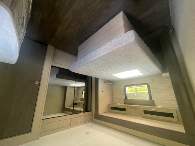 Inside this RV rental: a comfortable living space with two bunks, window view, and built-in storage. Ideal for travel.. Forest River Coachmen Aurora 2023