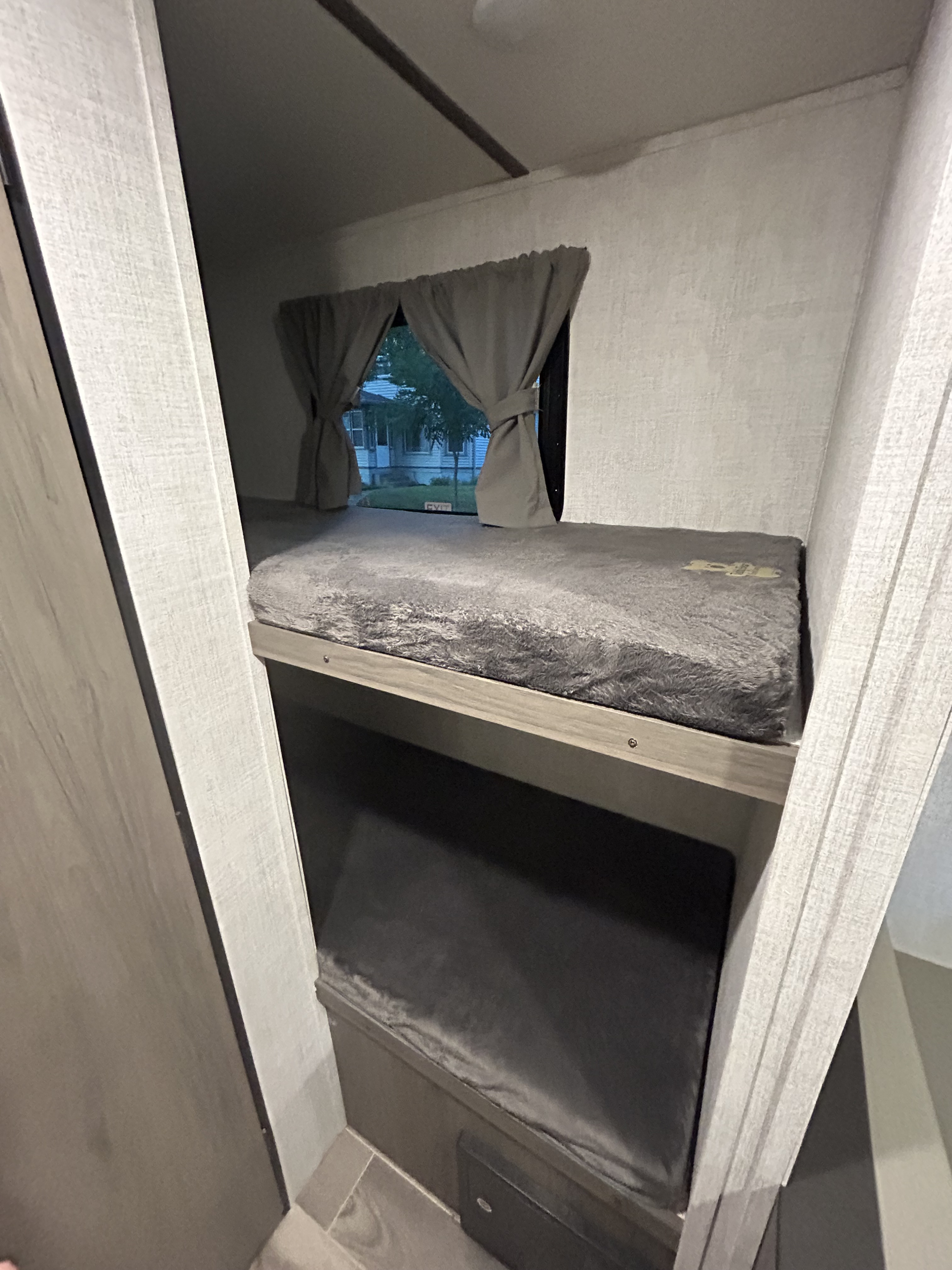Interior of an RV rental showing two cozy bunk beds with plush grey bedding, and a window with curtains offering an outside view.. Gulf Stream Ameri-Lite Super Lite 2021