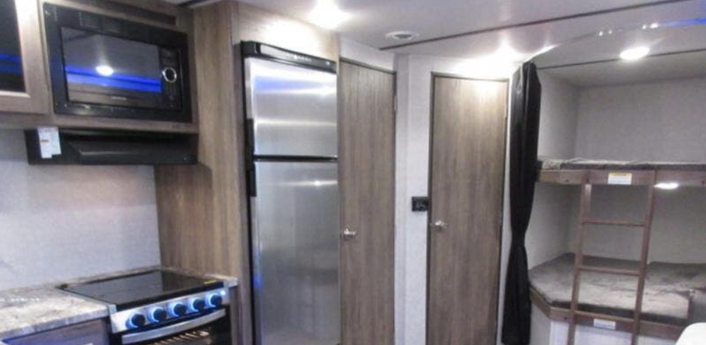 rv rental: Interior view of a well-equipped kitchen with microwave, stove, and fridge, adjacent to cozy bunk beds.. Sportsmen Sportsmen SE 2020