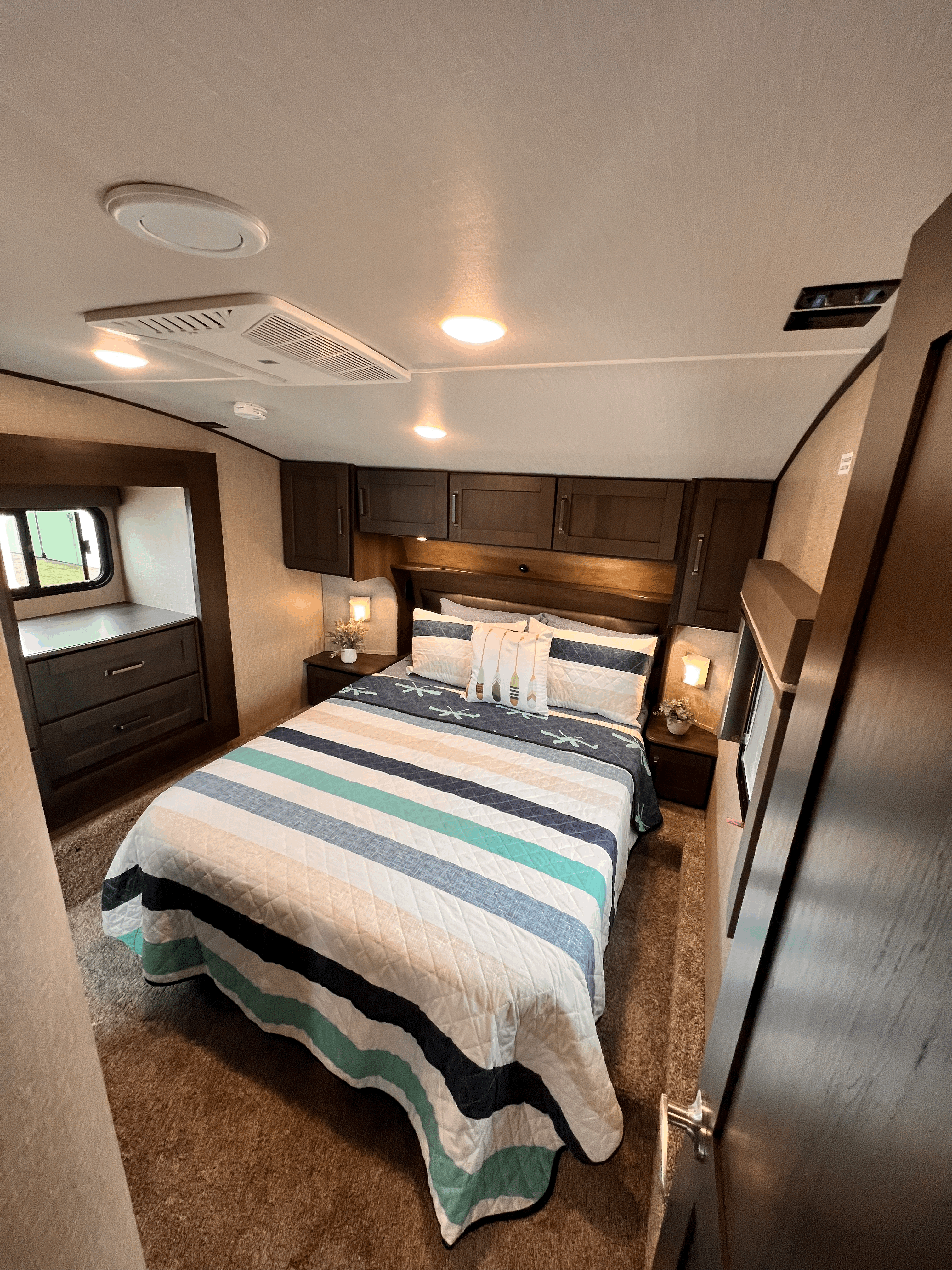 Spacious RV rental bedroom with a striped bed, overhead storage, AC, and lighting for cozy travel.. Grand Design Reflection 2023