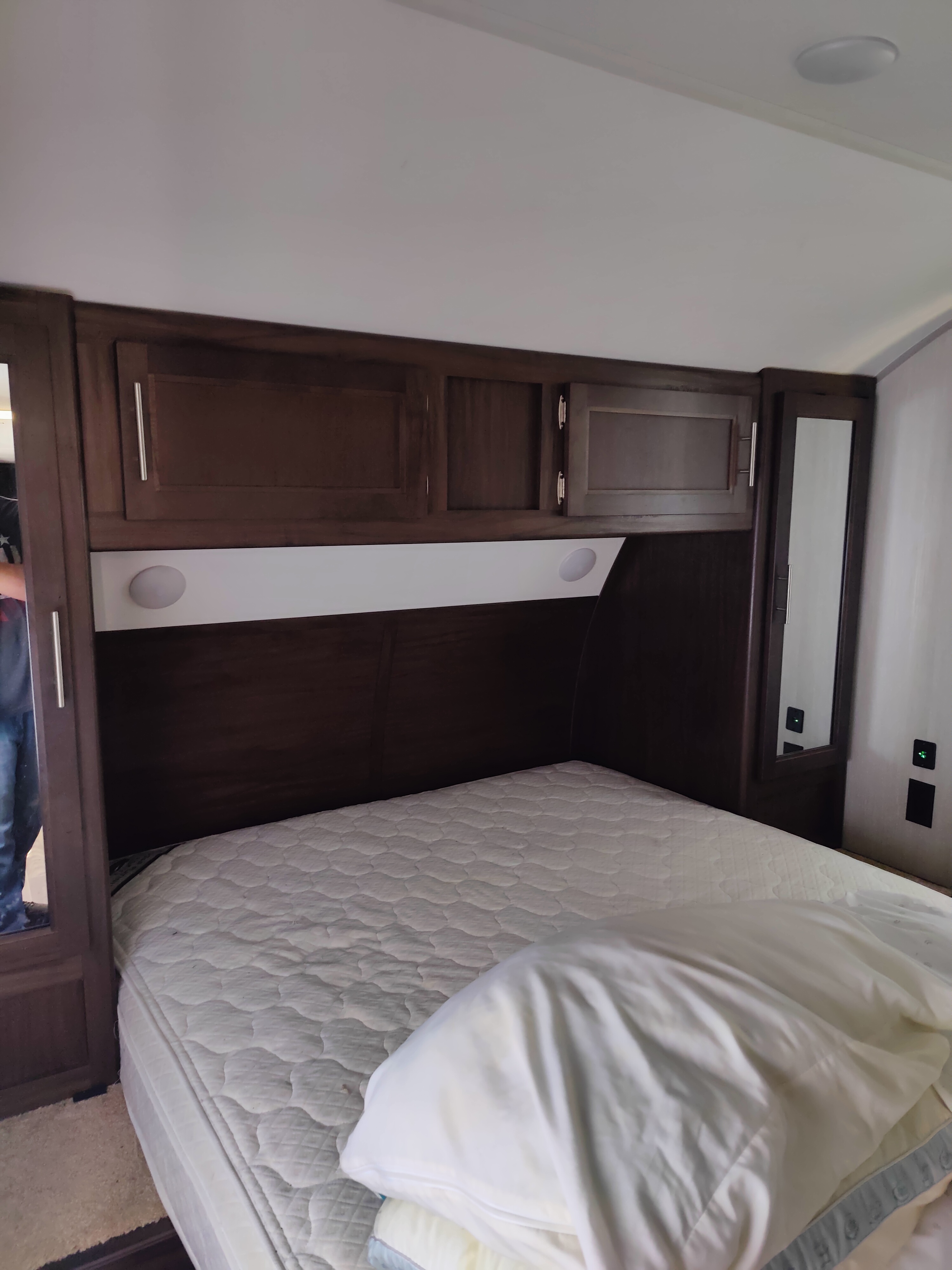 Inside an RV rental: a cozy bedroom with a clean mattress, dark wood cabinets, and integrated mirrors.. Forest River Cherokee 2019
