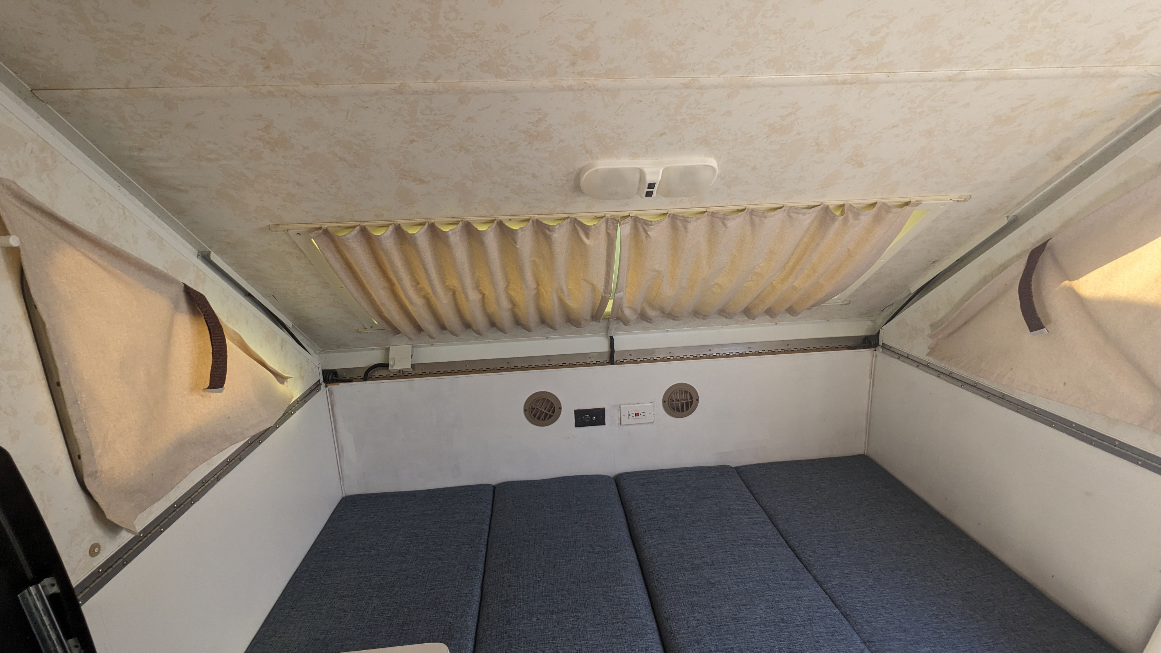 This RV rental's interior features a compact bed, privacy curtains, vents, and an overhead light.. Chalet Chalet Popup Trailer 2006