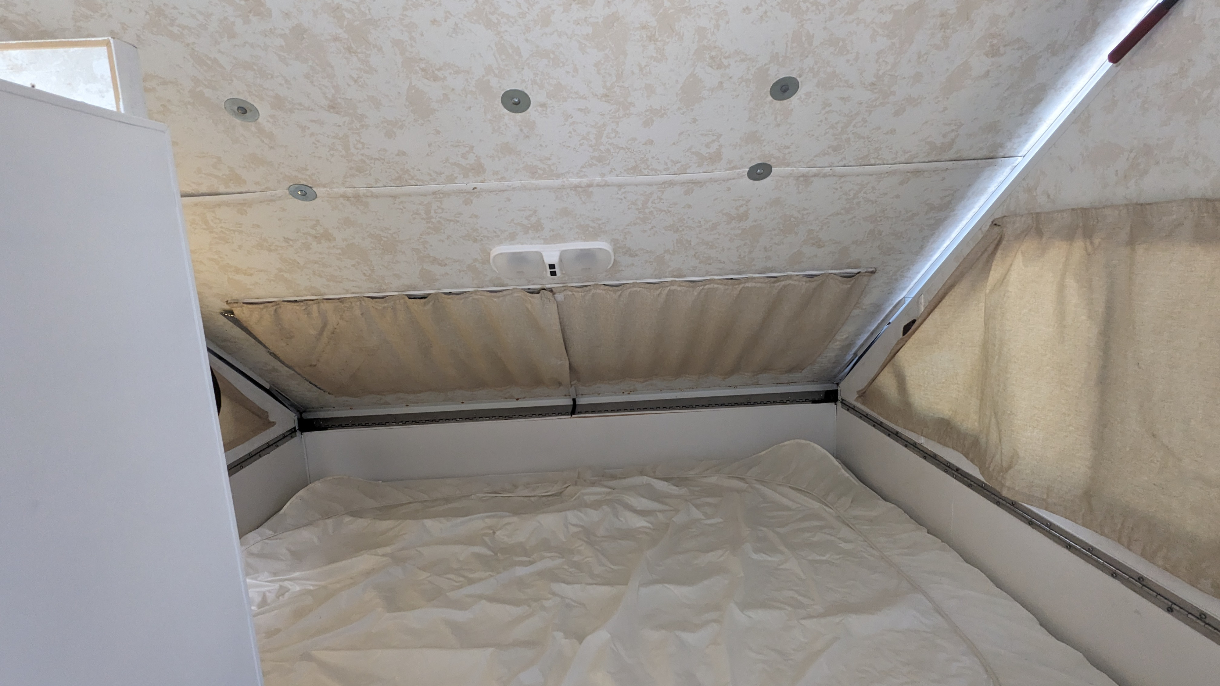 Inside an RV rental: a neat bed with white sheets, overhead light, and side curtains for privacy. Ideal for compact adventures.. Chalet Chalet Popup Trailer 2006