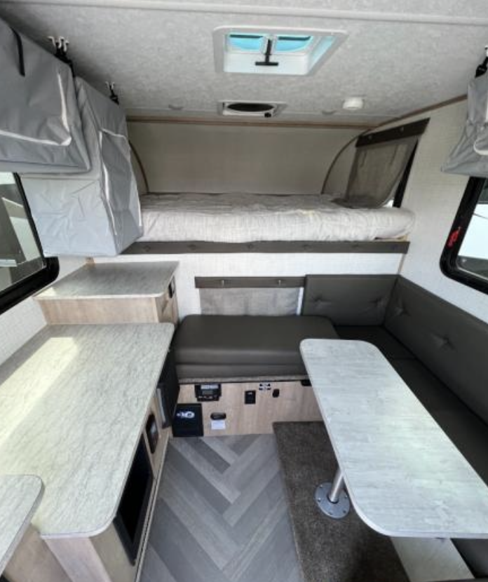 RV rental interior: cozy overhead bed, versatile dinette, and kitchenette area. Ideal for compact adventures.. Palomino Backpack Edition 2023