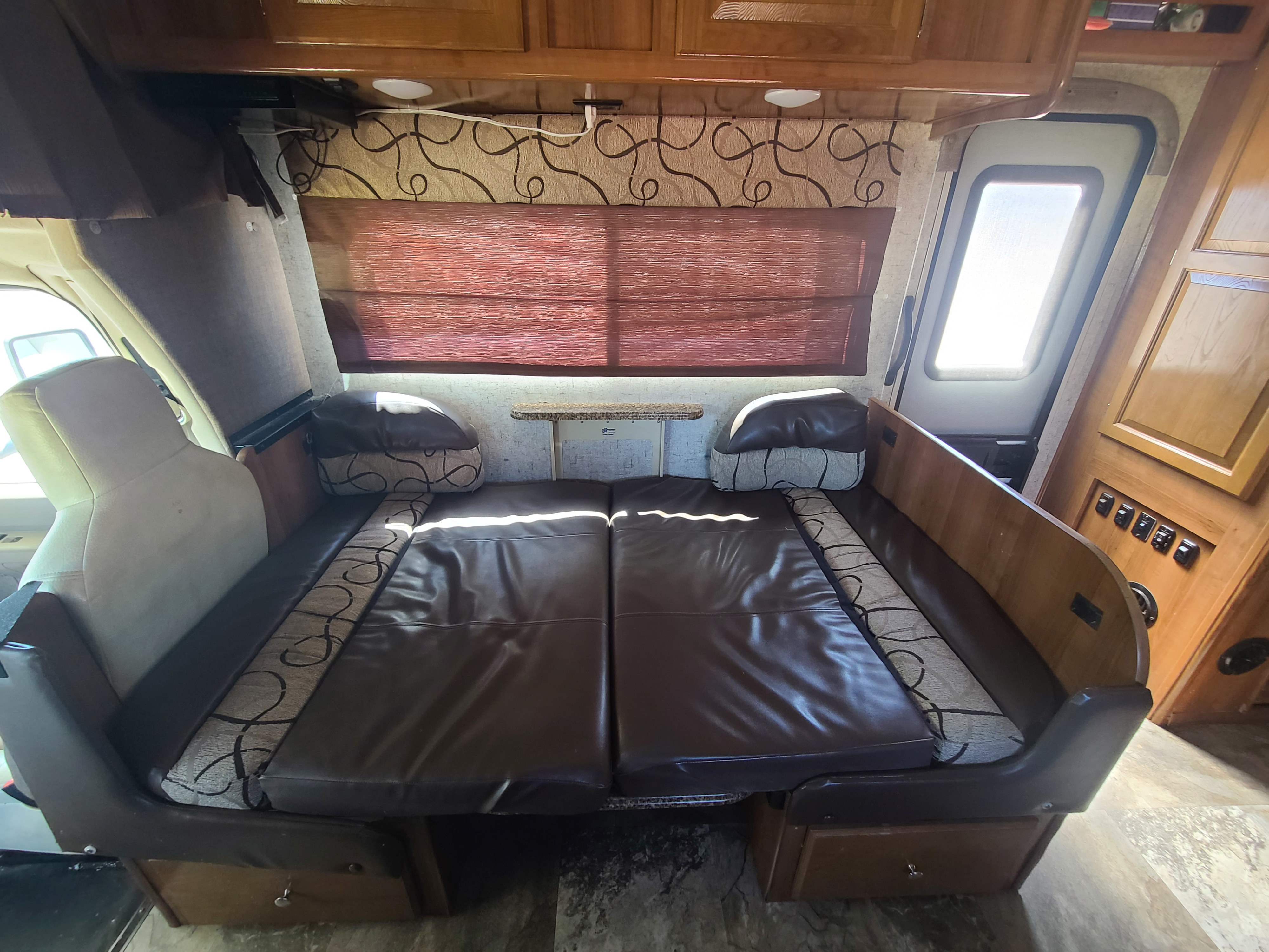Spacious RV rental interior with convertible seating/bed, wooden cabinets, and window shade for comfortable travel.. Forest River Coachmen Leprechaun 2018