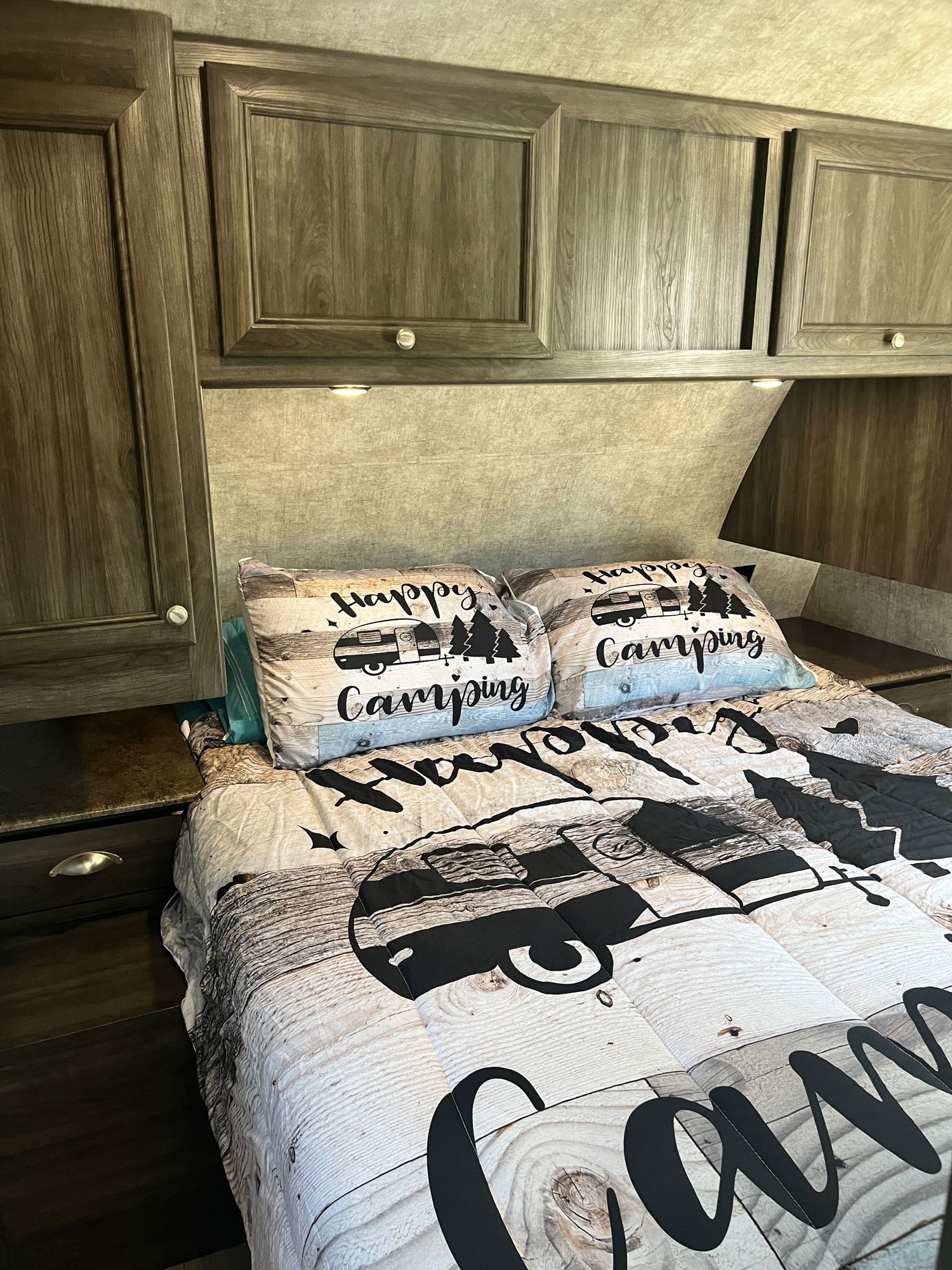 Cozy RV rental interior with "Happy Camping" bedding, wood-look cabinets, and a comfortable bed.. Highland Ridge RV Light 2017