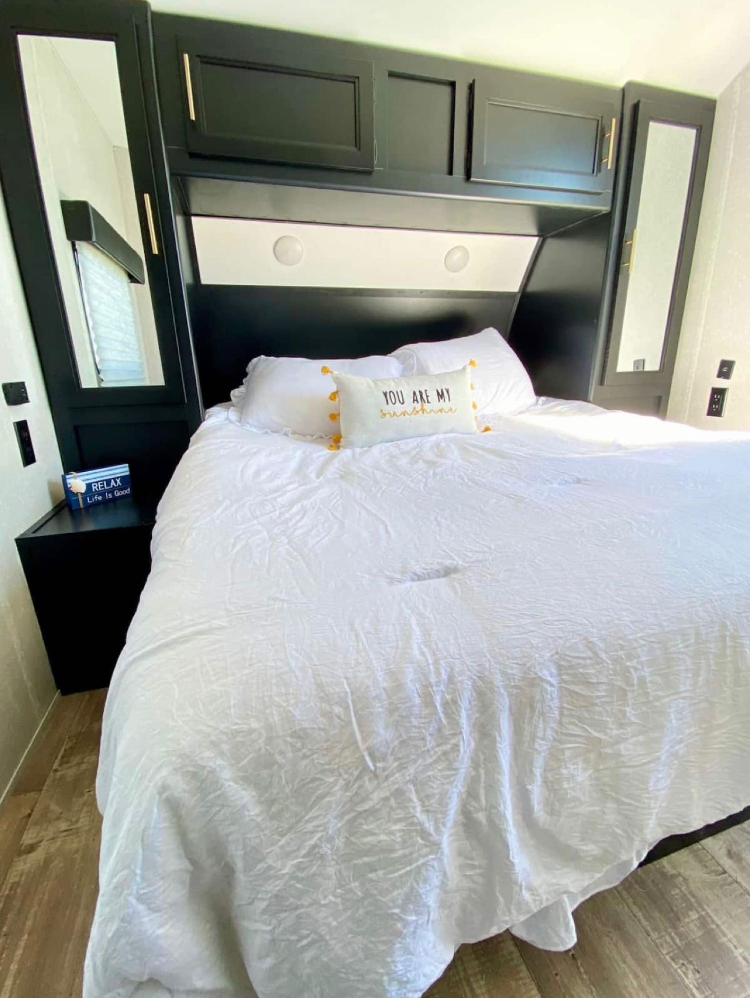 Bright RV rental bedroom features a comfy queen bed, black headboard with mirrored cabinets, and built-in storage.. Forest River Cherokee 264DBH 2021