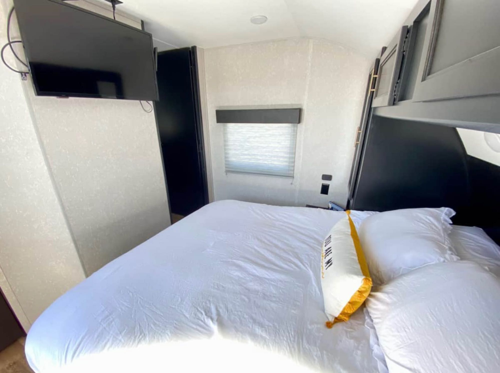 Cozy RV rental bedroom features a large bed with white linens, wall-mounted TV, window, and overhead storage.. Forest River Cherokee 264DBH 2021