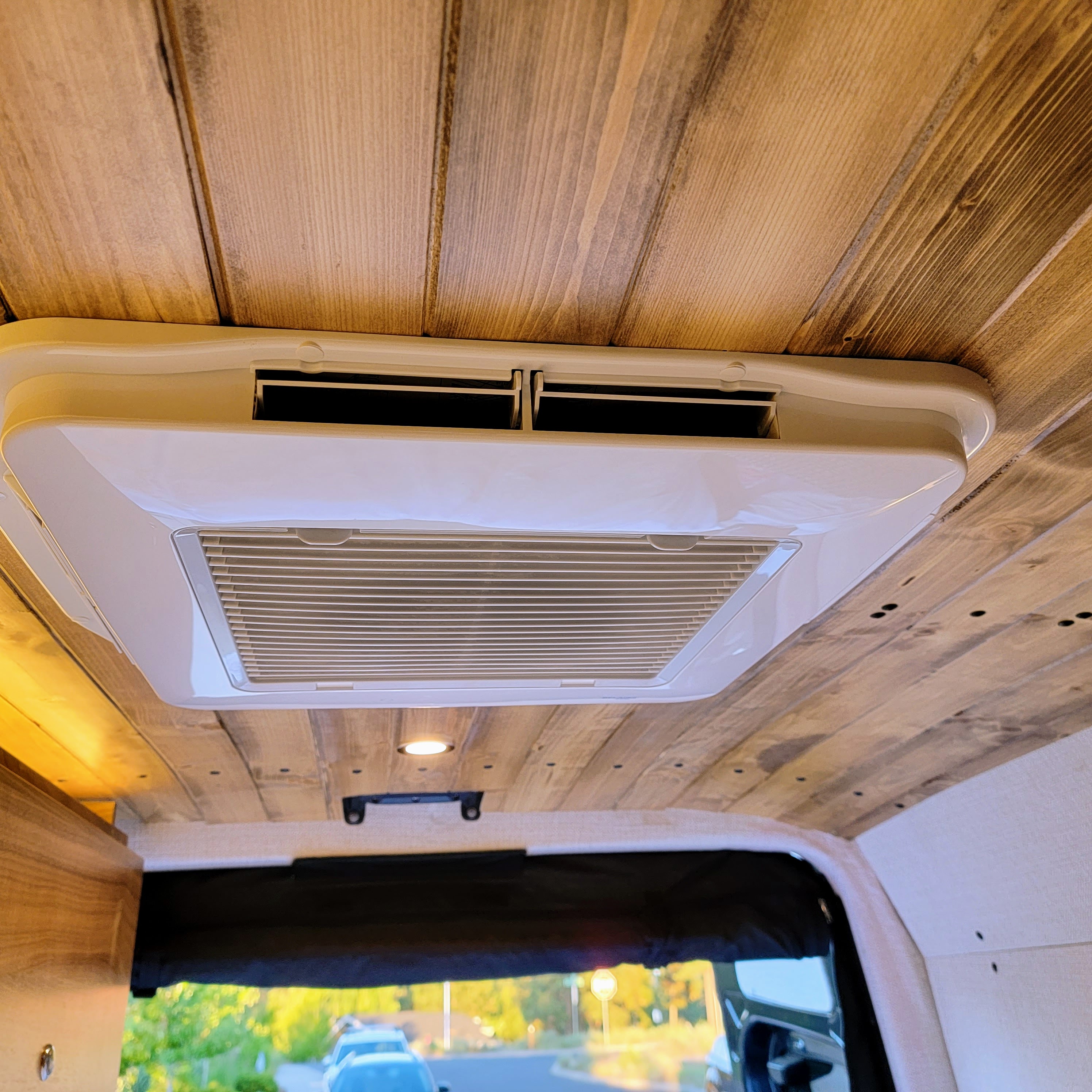 Inside an RV rental: a white roof-mounted AC unit provides climate control in this cozy space with a rustic wooden ceiling.. Mercedes-Benz Sprinter 2020