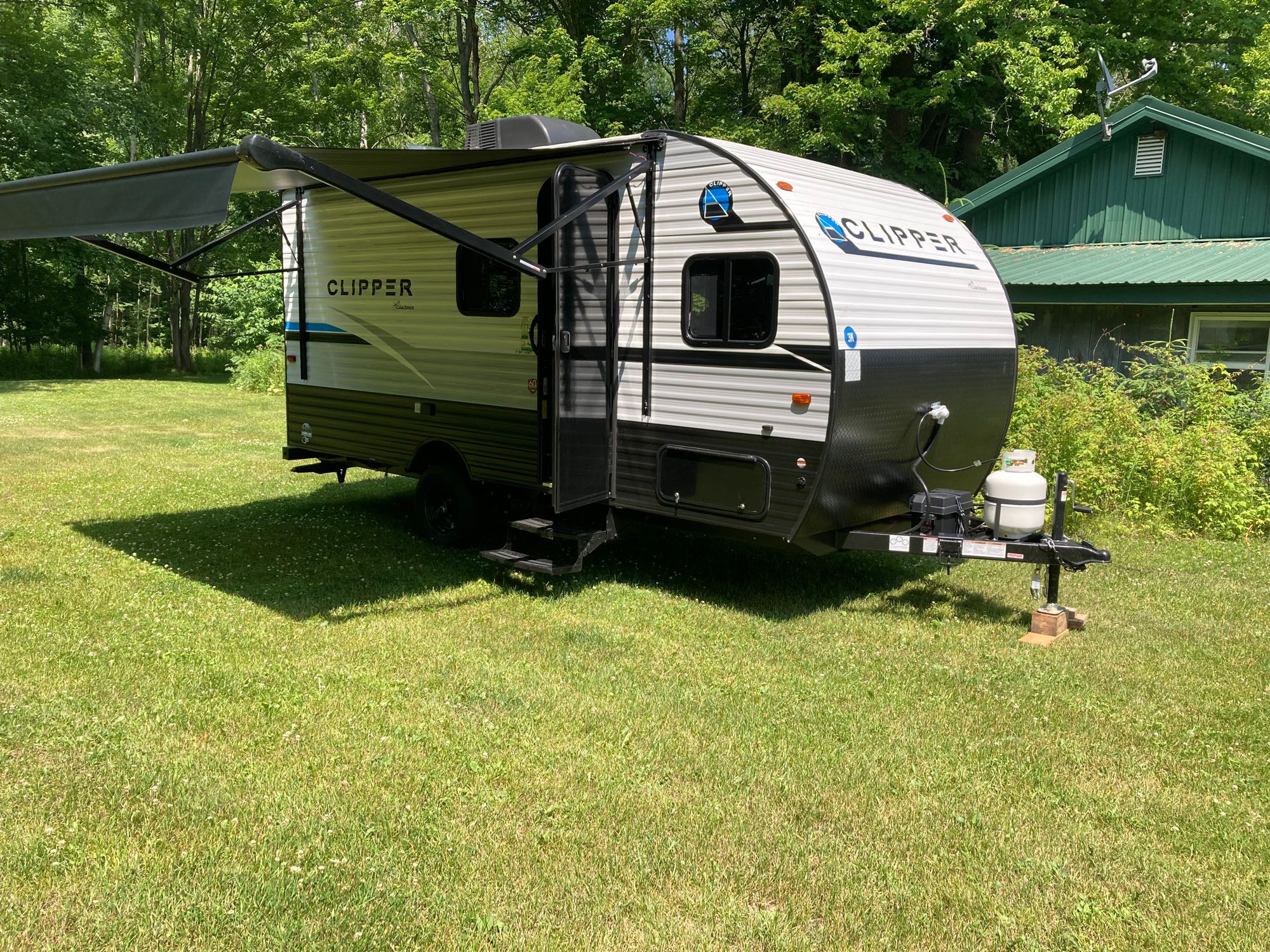White and black travel trailer with extended awning for RV rental, parked on lush green grass on a sunny day.. Coachmen Clipper 17CBH 2023