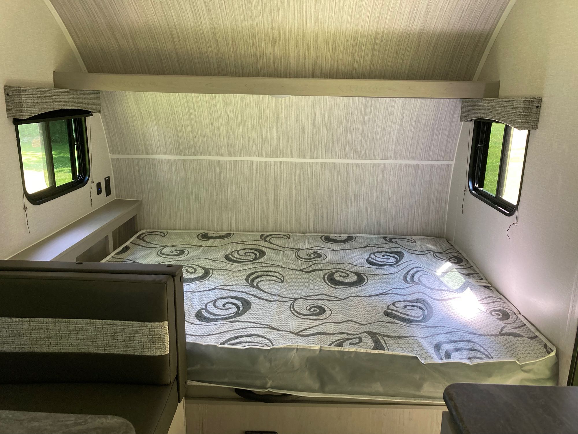 Compact RV rental sleeping area: a comfortable bed with a patterned mattress, light wood-grain walls, and dual windows.. Coachmen Clipper 17CBH 2023