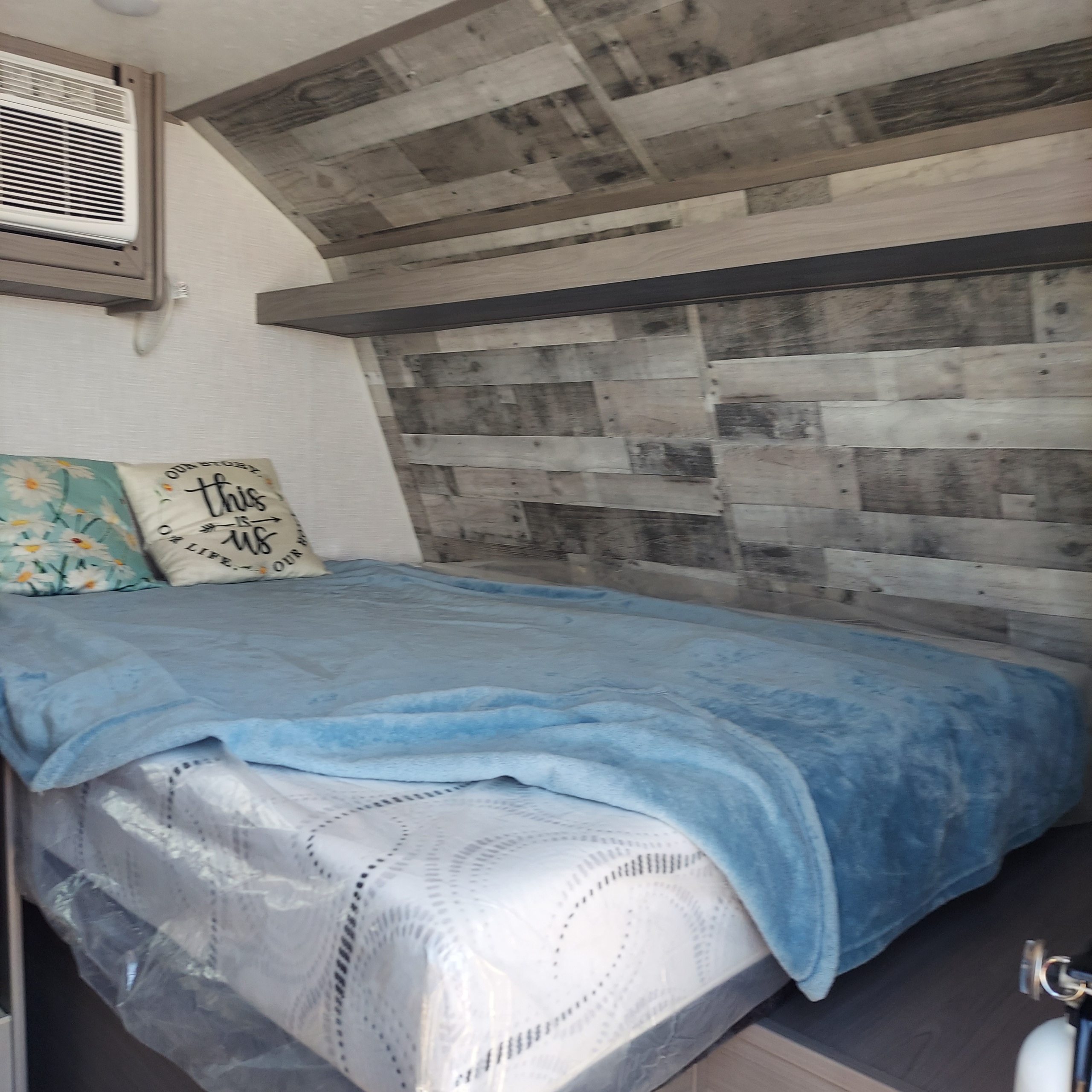 An inviting RV rental bedroom with a blue-blanketed bed, decorative pillows, wall AC, and stylish wood-look paneling.. Dutchmen Coleman Lantern LT 2023