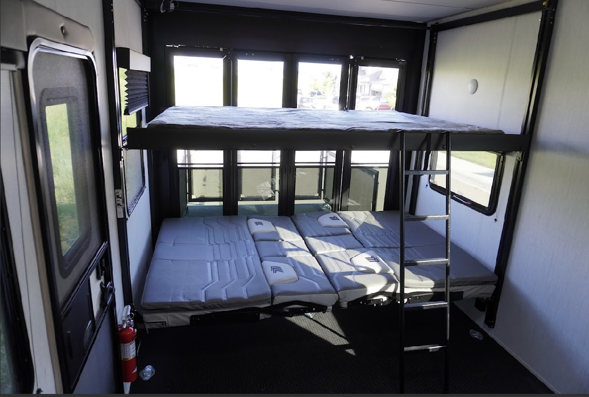Spacious RV rental interior with a stacked bunk bed system and convertible lower sleeping/seating area. Fire extinguisher visible.. Grand Design Momentum 2023