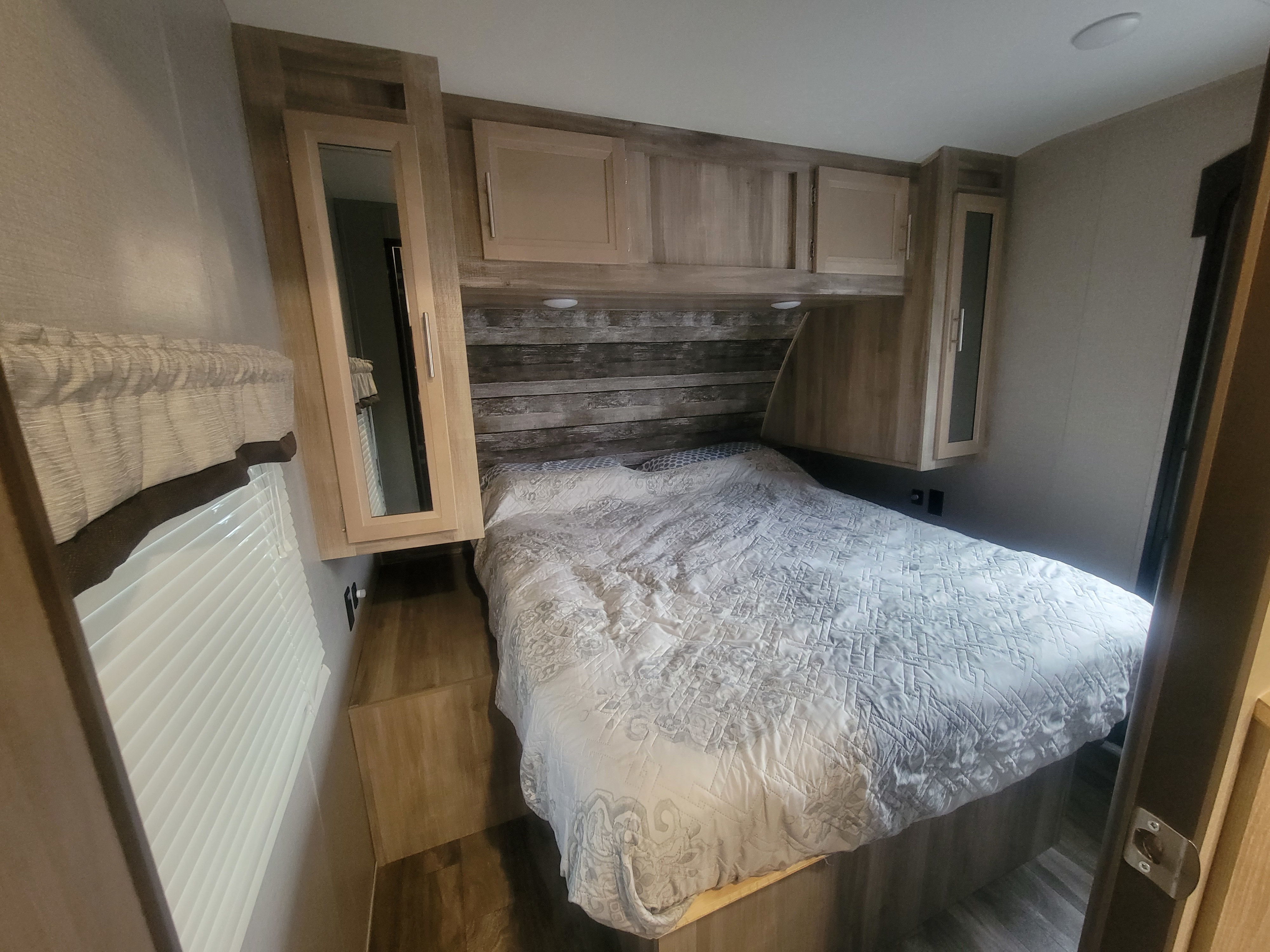 RV rental bedroom with a cozy bed, wood accents, overhead cabinets, and window blinds, designed for comfortable travel.. Forest River Coachmen Catalina Legacy 2021