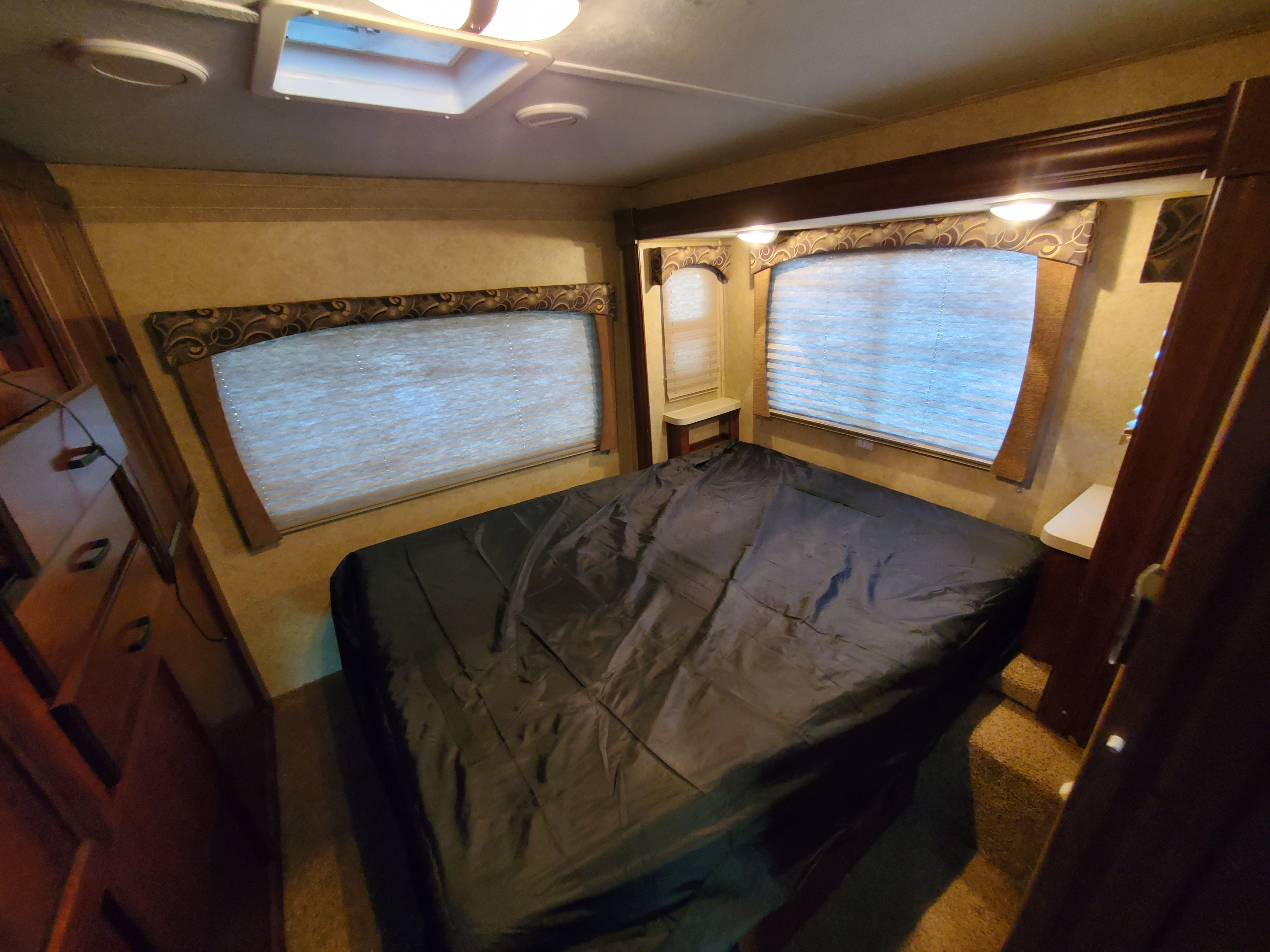 Comfortable RV rental bedroom featuring a large bed with dark bedding, multiple windows, and built-in storage.. Forest River Sunseeker 2014