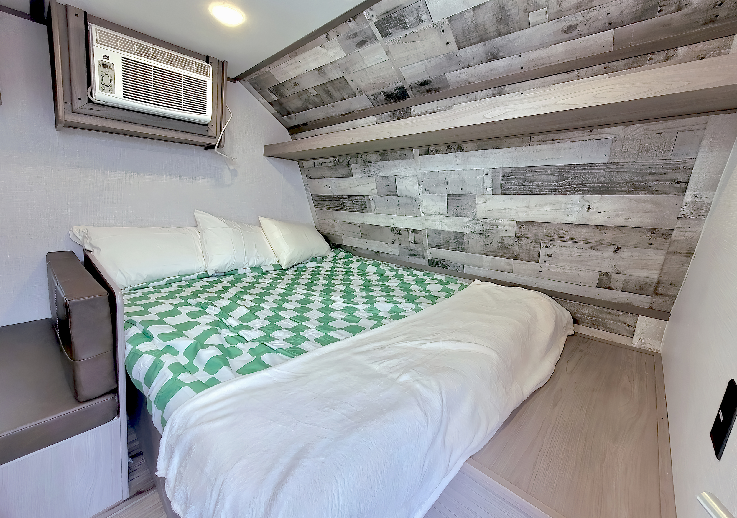 Cozy RV rental bedroom featuring a comfortable bed with a green and white comforter, wall-mounted AC, and rustic wood paneling.. Coleman Lantern 2023