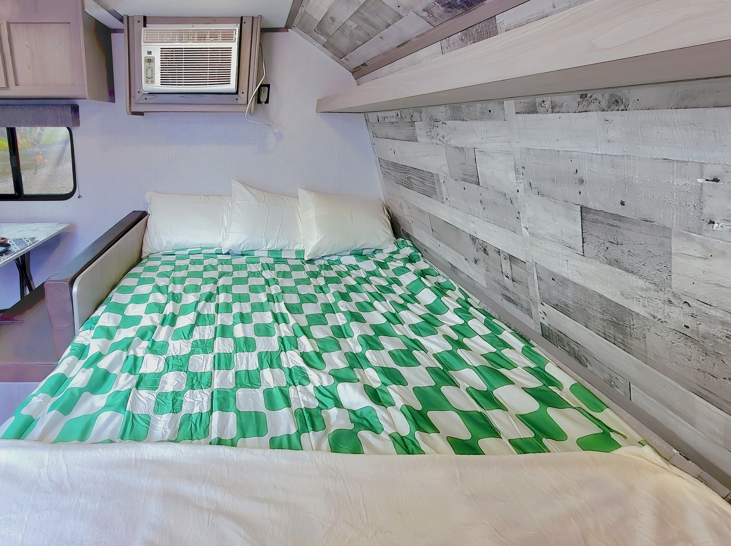 Cozy RV rental interior featuring a bed with green checker comforter, window view, and AC unit.. Coleman Lantern 2023