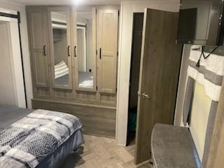 This RV rental bedroom features a large light wood wardrobe with mirrored doors, a cozy bed, and a wall-mounted TV for comfortable travel.. Forest River Puma 2021