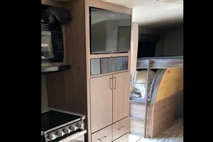 This RV rental's interior features a compact kitchen with a stove, TV, & built-in bunk beds for travel.. Grand Design Imagine 2022