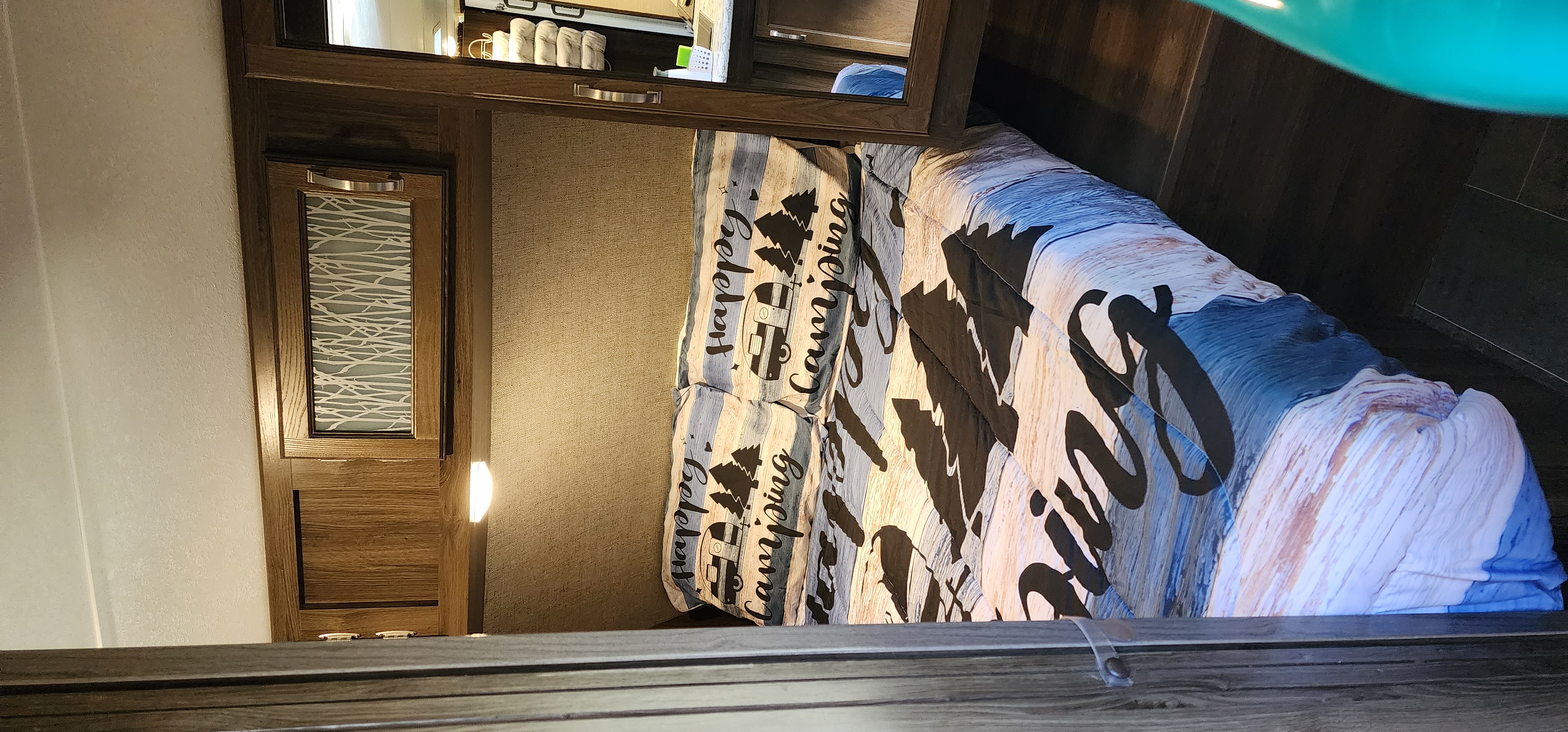 Cozy RV rental bedroom with a "Happy Camping" comforter on the bed, detailed wooden cabinets, and a mirrored wall.. Keystone RV Bullet Ultra Lite 2018