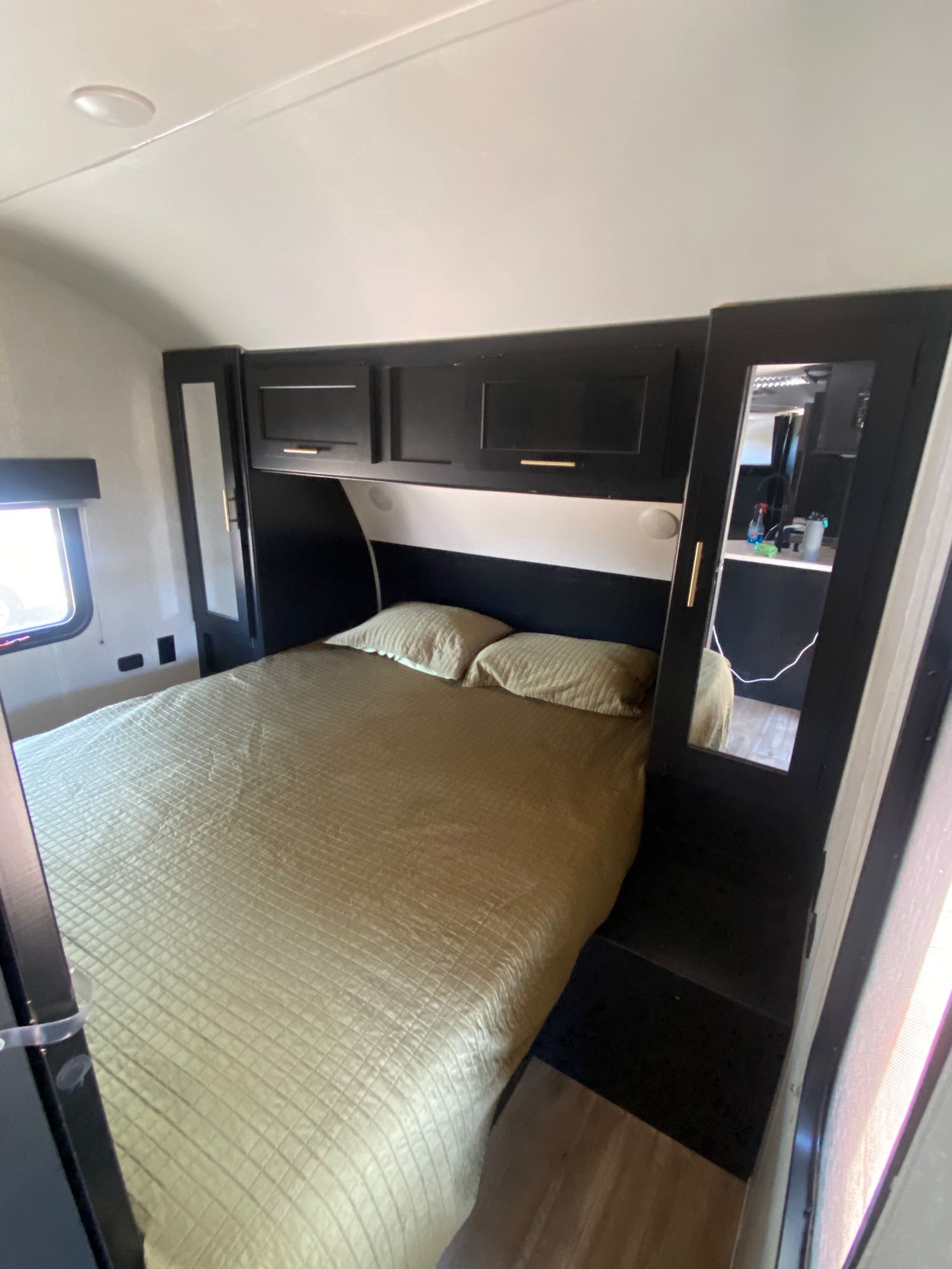 Spacious bedroom in an RV rental, featuring a queen bed with olive comforter, dark cabinetry, and mirrored closets.. Forest River Cherokee Grey Wolf 2021