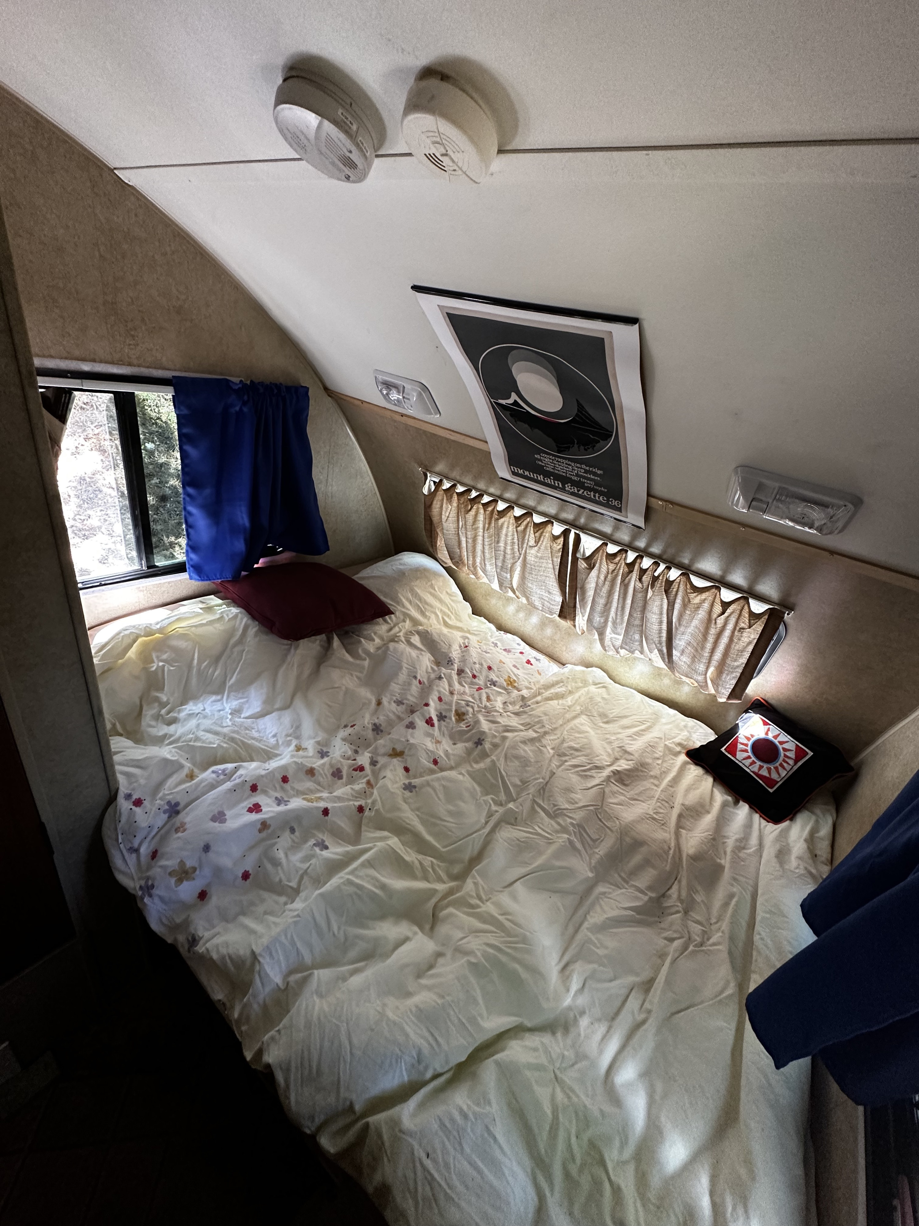 Cozy RV rental sleeping area: a comfortable bed with floral sheets, windows, ceiling alarms, and a unique poster for mobile comfort.. R-Pod R-Pod Trailer 2011