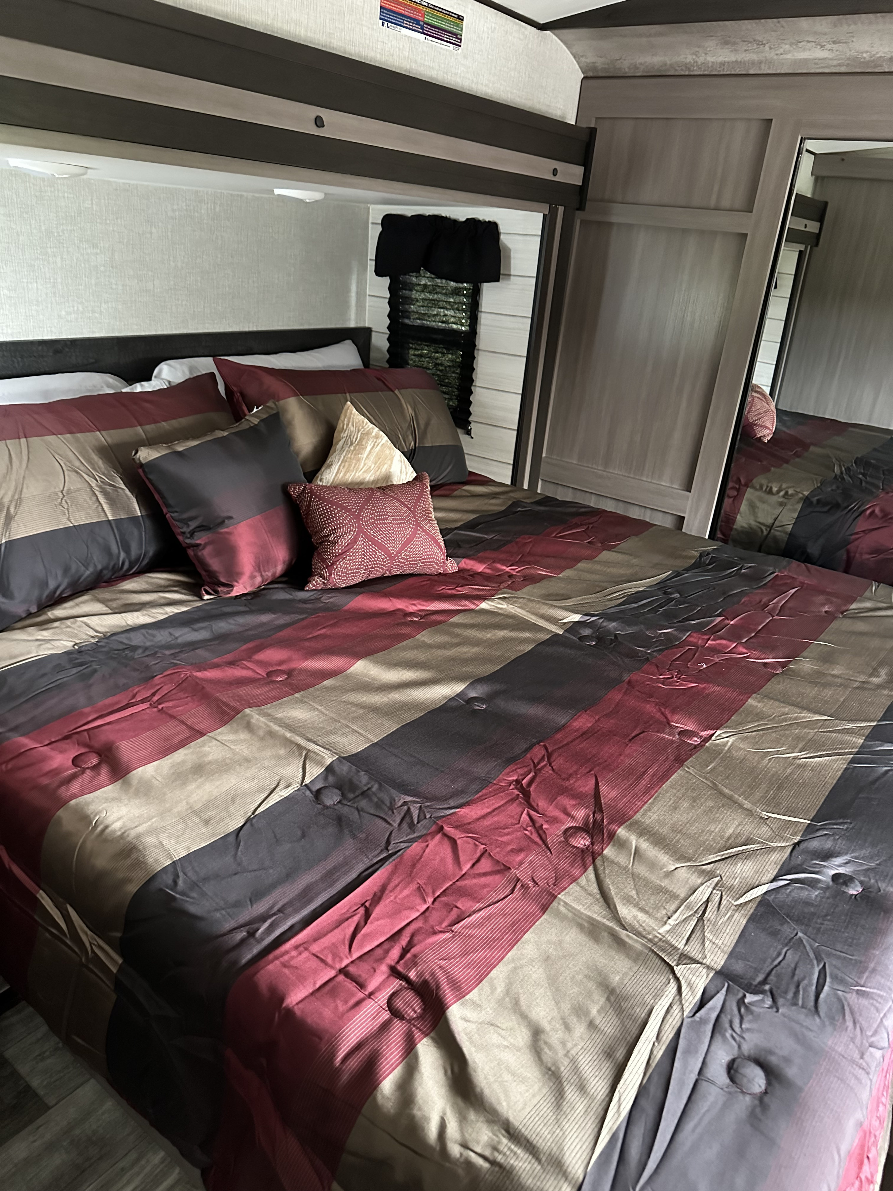 Comfortable RV rental bedroom featuring a striped bed in maroon, gray, and tan. Perfect for your travels!. Crossroads RV Sunset Trail Super Lite 2023