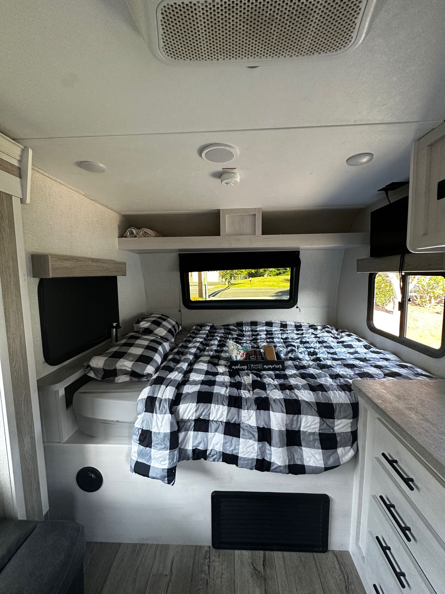 Cozy RV rental bedroom with black and white buffalo check bedding. The modern space features windows showing outdoor scenery, perfect for making memories.. Dutchmen Coleman Rubicon 2021