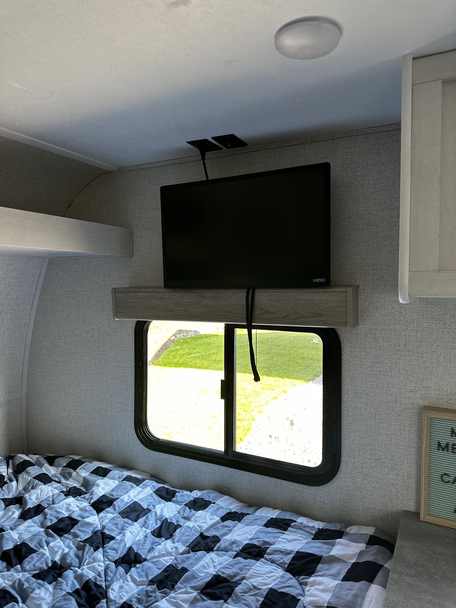 Cozy RV rental bedroom featuring a bed with buffalo plaid comforter, mounted TV, and window view of the outdoors.. Dutchmen Coleman Rubicon 2021