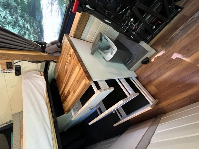 Inside a modern RV rental: compact camper van interior with a bed, wooden table, and smart storage solutions.. Mercedes Sprinter 2016