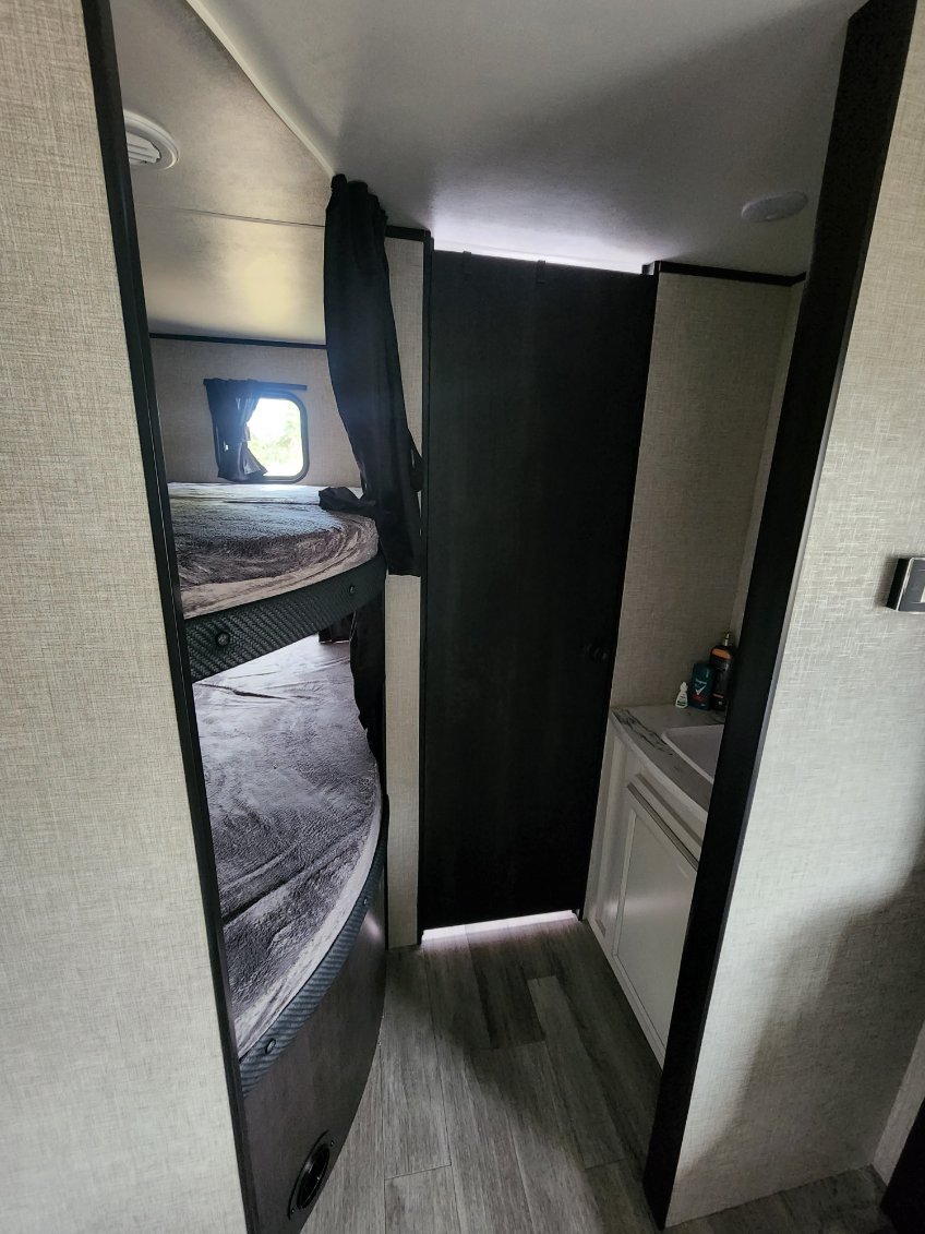 Compact RV rental interior: bunk beds on left, dark bathroom door, and small sink vanity on the right.. Jayco Jay Flight SLX 2022