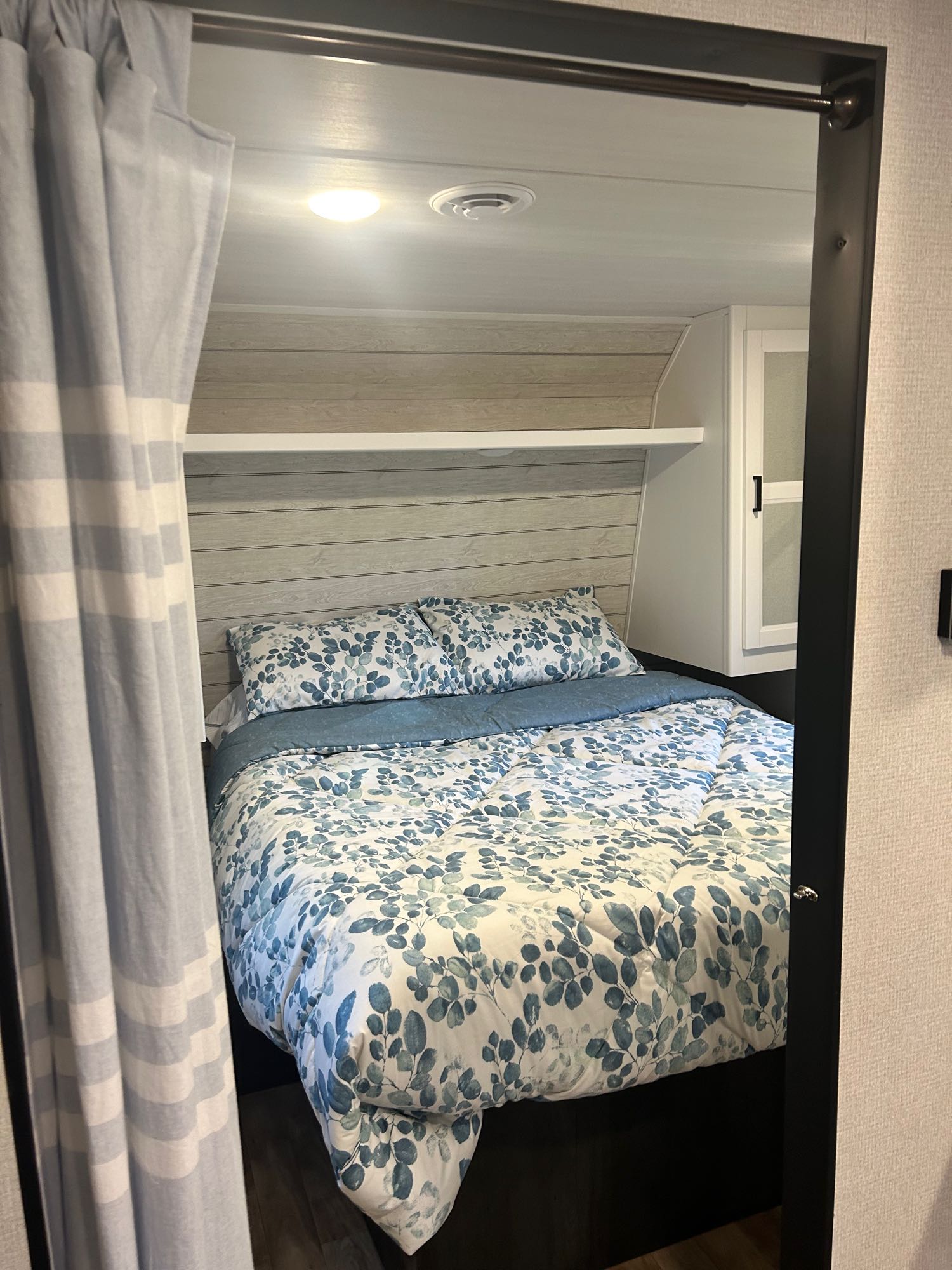 Inside a cozy RV rental bedroom: bed with blue leaf-patterned duvet, light wood accent wall, and built-in storage.. Keystone RV Hideout 2022