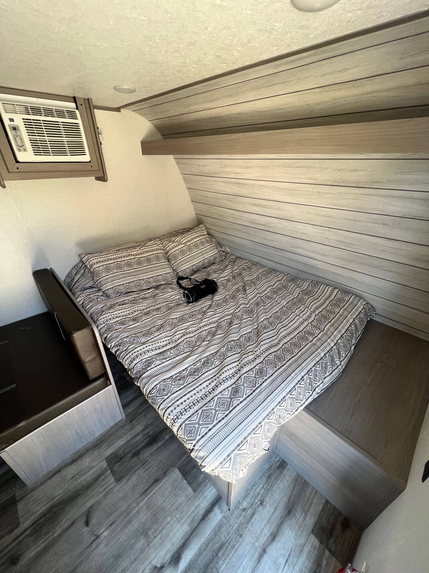 Cozy RV rental bedroom featuring a patterned bed, mounted AC unit, and built-in storage, ideal for travel and camping.. Dutchmen Coleman Lantern LT 2023