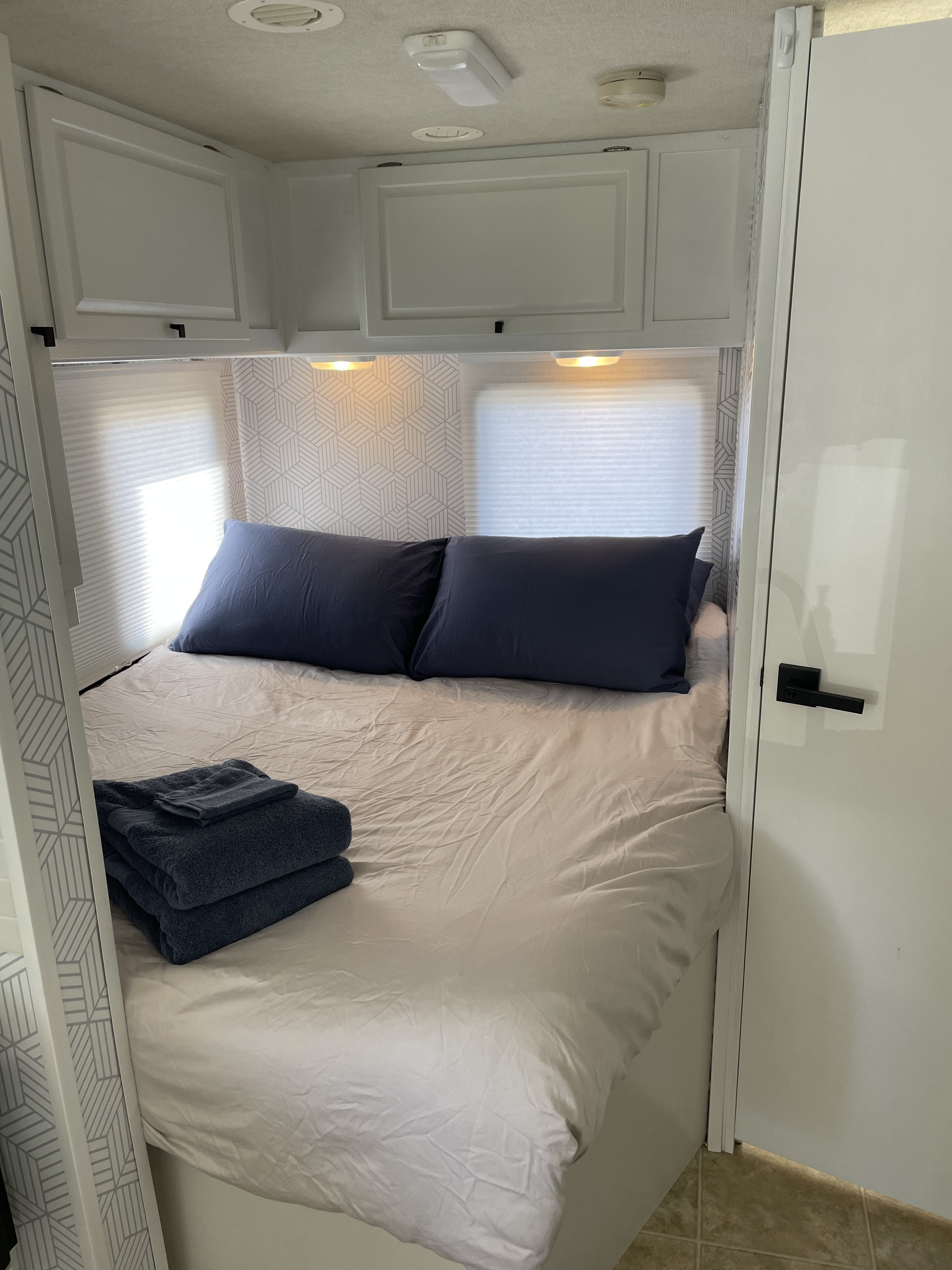 Explore this modern RV rental bedroom with blue pillows, folded towels, overhead cabinets, and unique geometric wallpaper.. Winnebago Access 2008