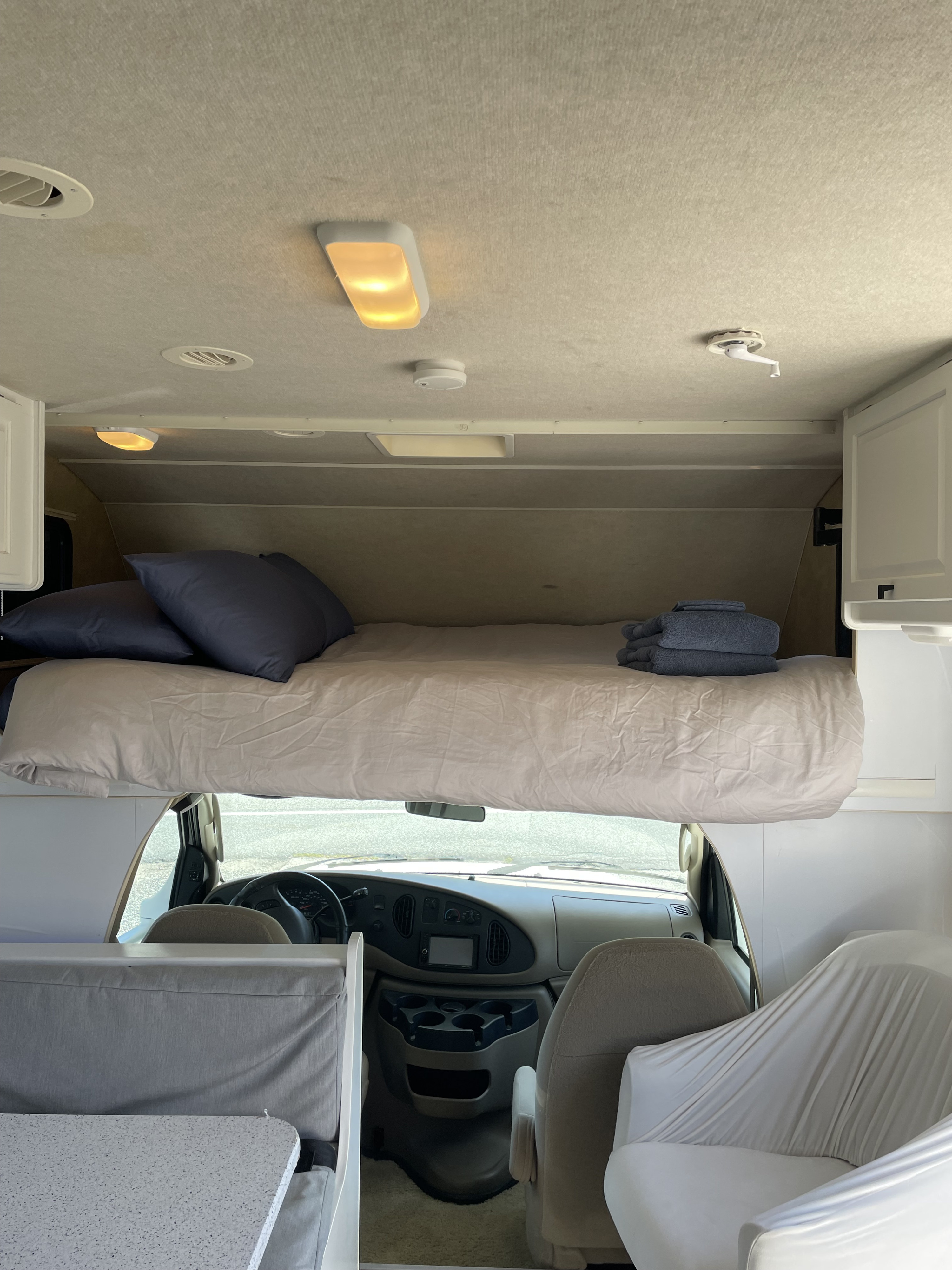 Cozy cab-over bunk bed inside an RV rental, showing the sleeping area and front cockpit for a comfortable journey.. Winnebago Access 2008