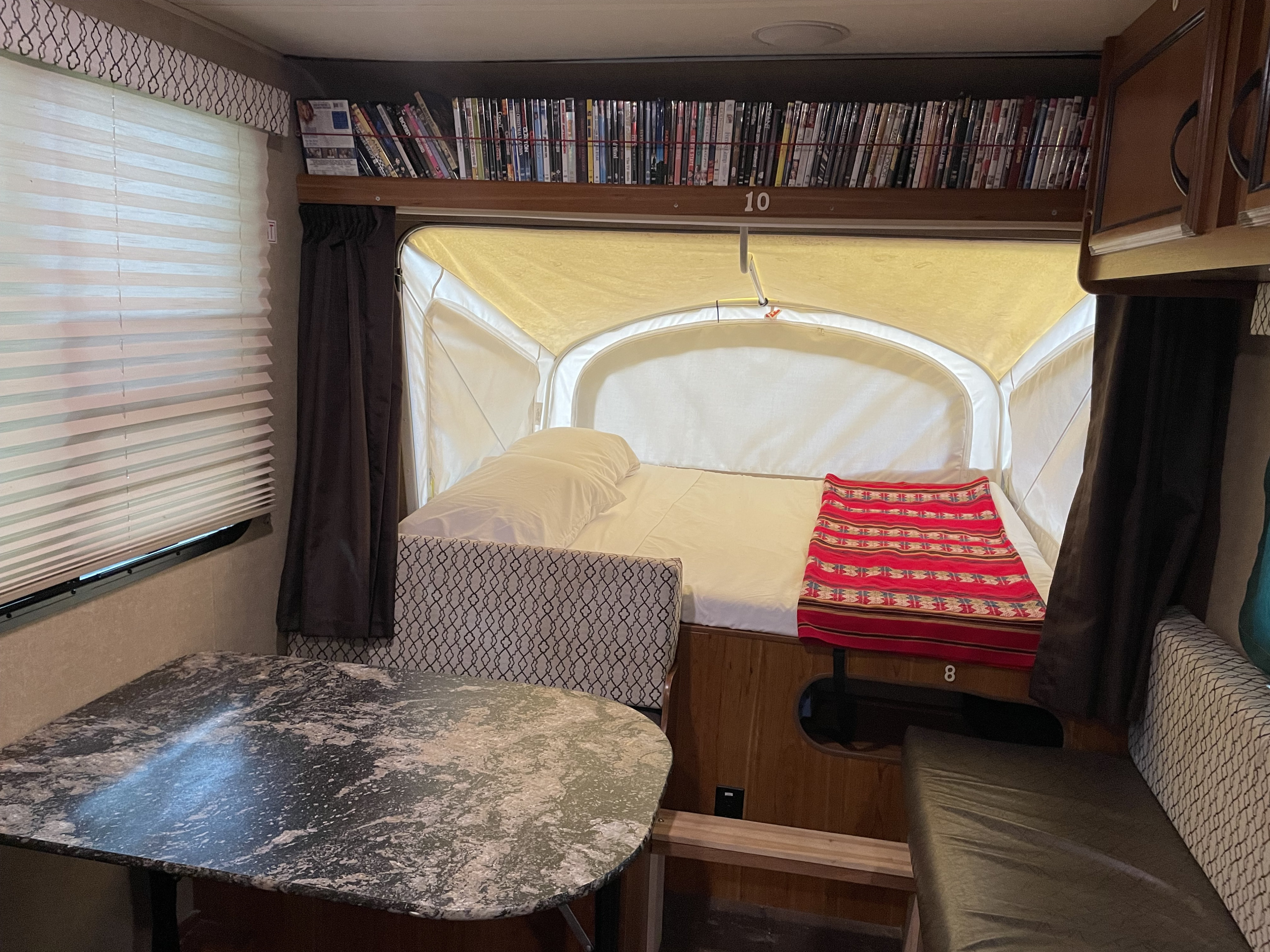 Inside an RV rental: a well-appointed space featuring a dining table, a pop-out bed, and DVD movie storage.. Starcraft Launch 2016