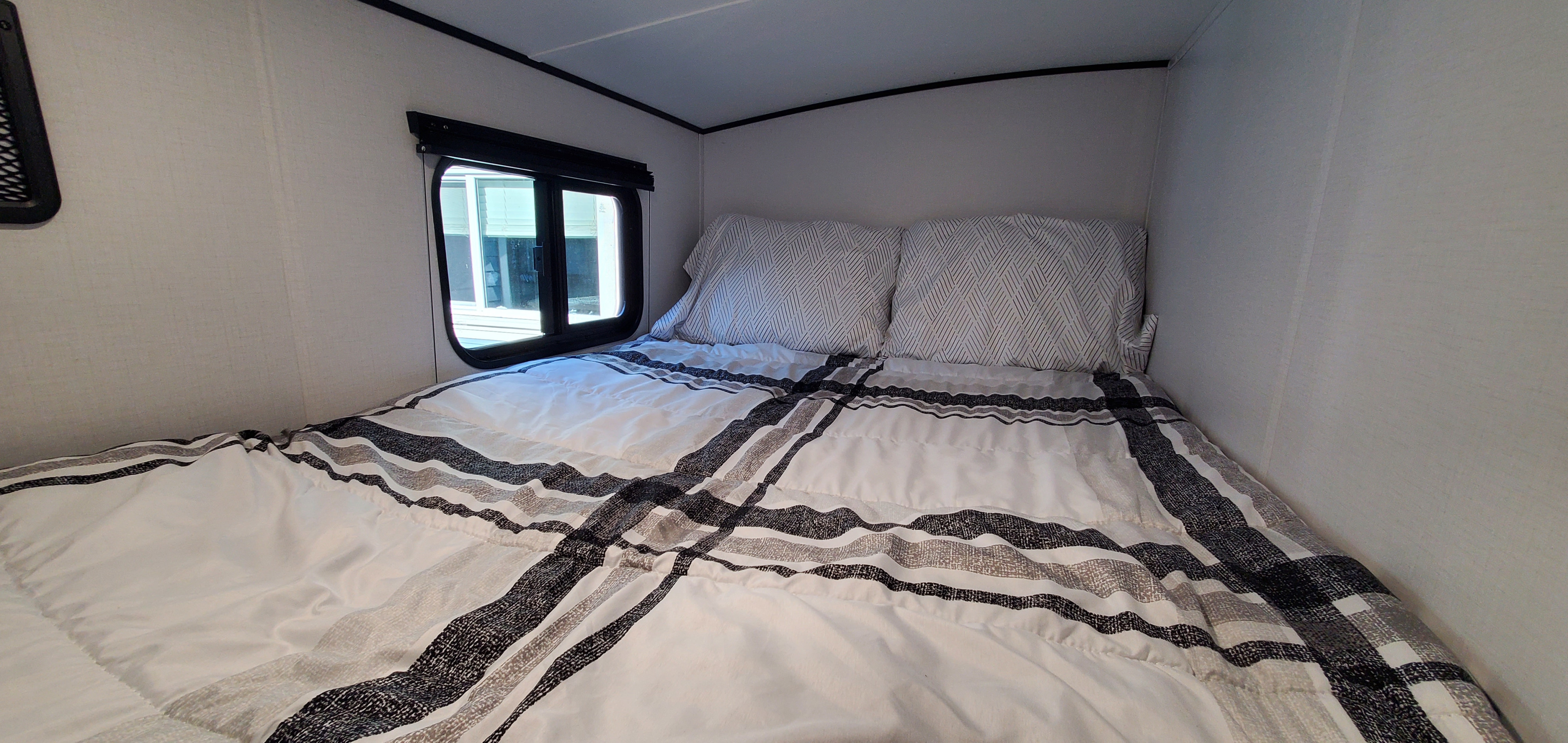 Inviting RV rental bedroom with a plaid/striped comforter, geometric pillows, and a window for natural light.. Keystone RV Springdale 2022