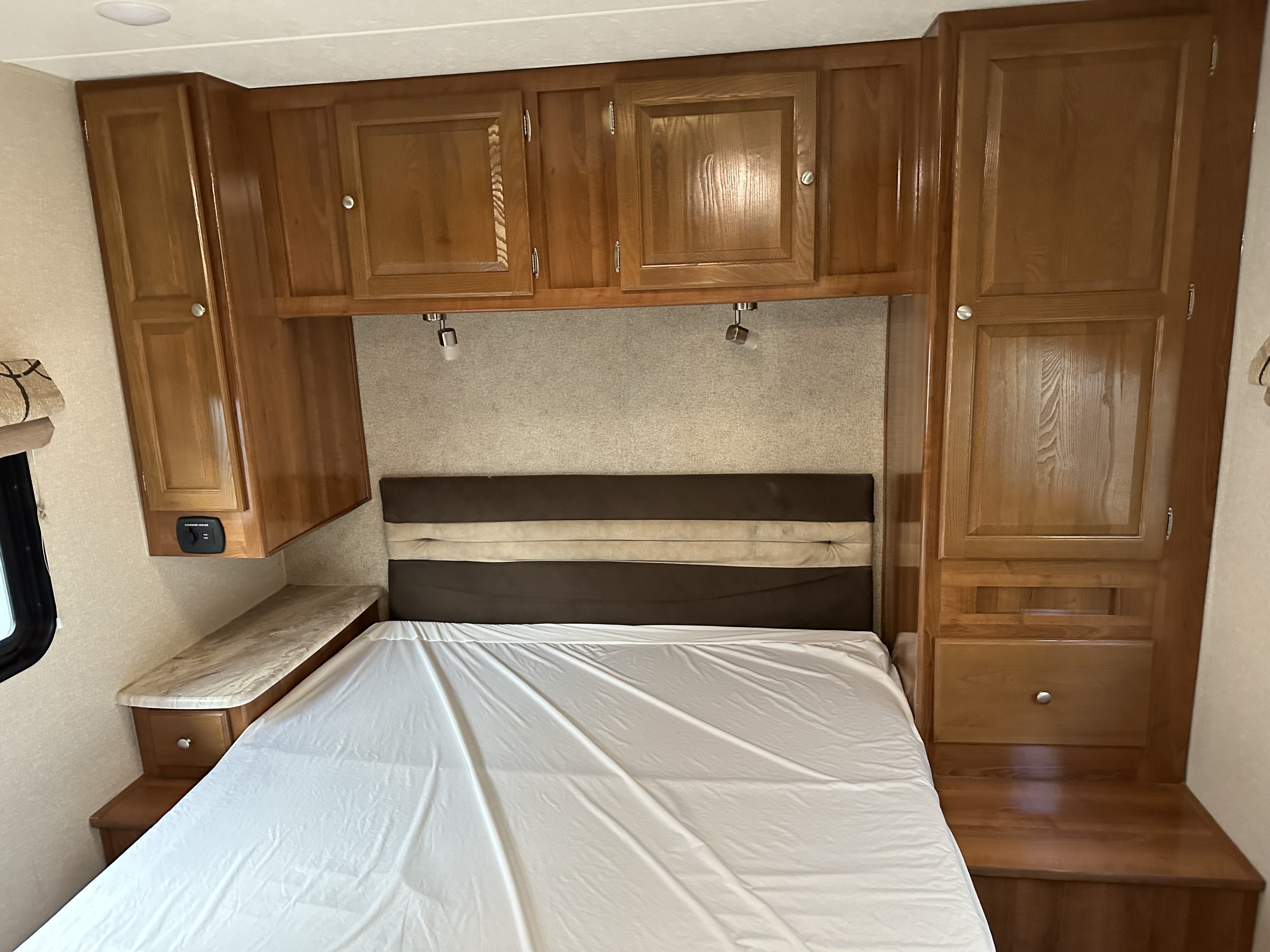 Clean RV rental bedroom with a bed, wooden overhead cabinets, and built-in storage. Ready for your adventure!. Coachmen Leprechaun 2019