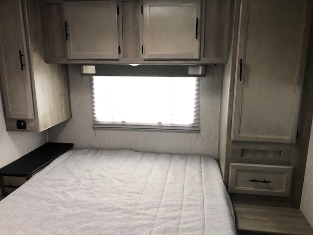 Inside an RV rental: a bright bedroom with bed, overhead cabinets, window, and built-in storage.. Coachman Freelander 2021