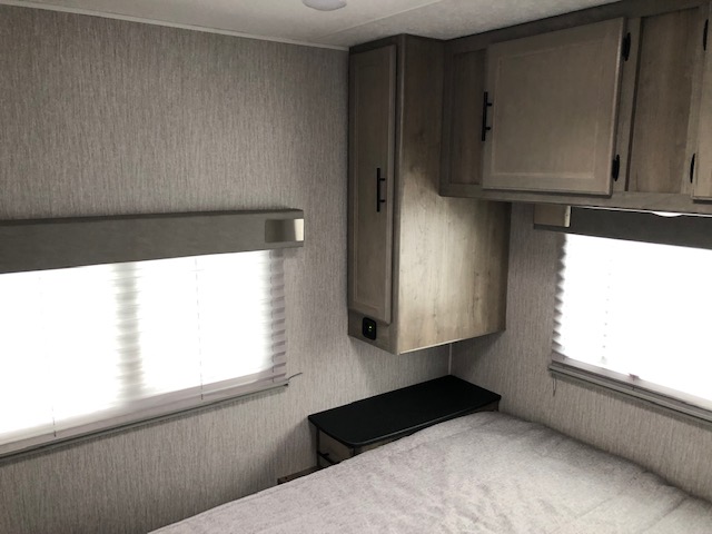 View of an RV rental bedroom featuring light grey textured walls, white blinds on windows, wooden cabinets, and a bed.. Coachman Freelander 2021