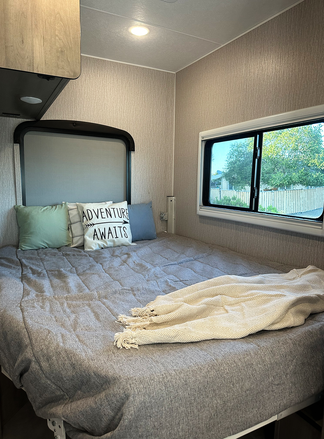 RV rental bedroom: a cozy bed with "ADVENTURE AWAITS" pillow, blanket, and window view.. Forest River Coachmen Cross Trail XL 2022