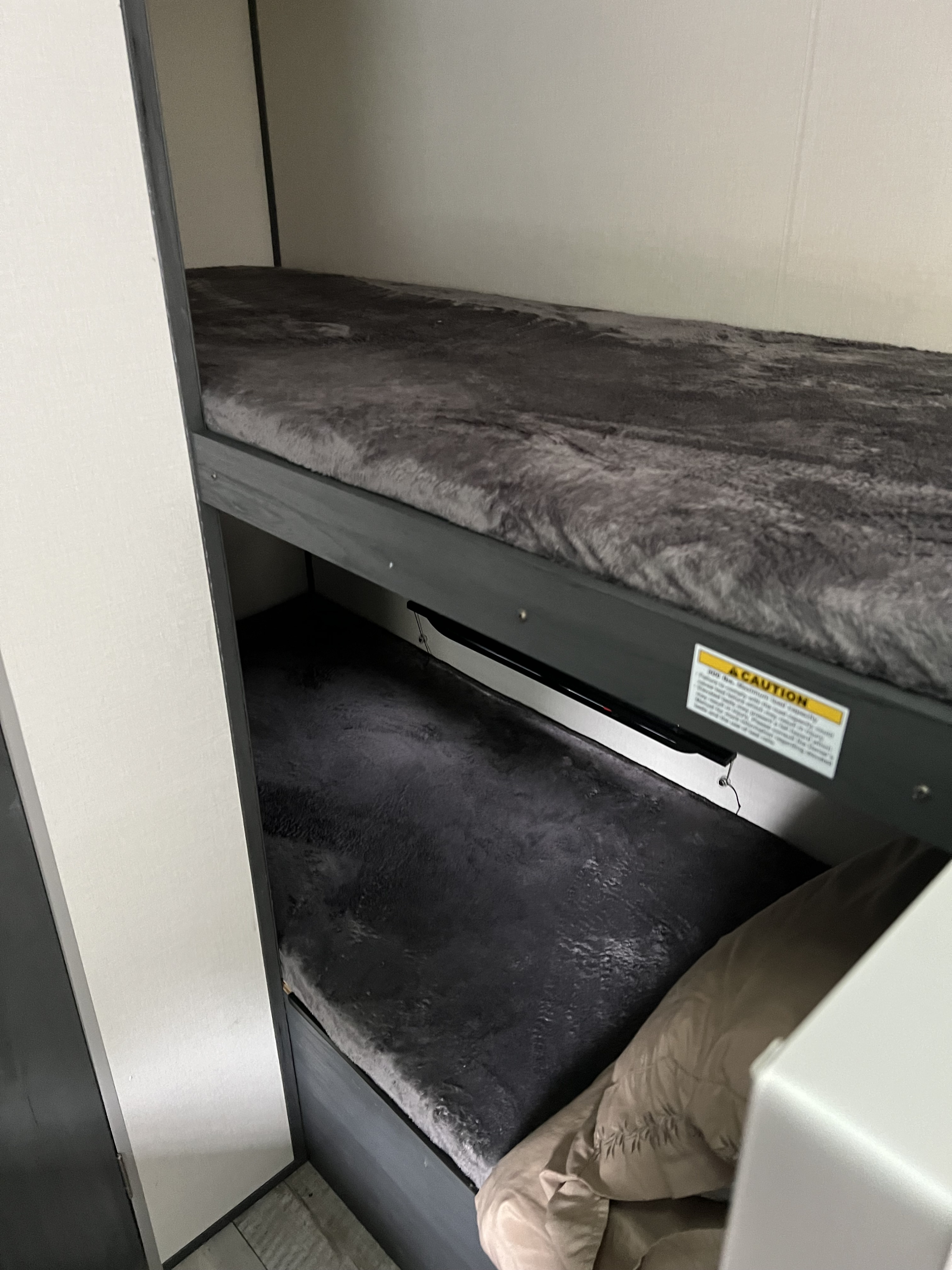 Cozy RV rental bunk beds feature soft gray bedding. A caution label is visible on the top bunk's frame.. Coachmen Aspen trail 2022