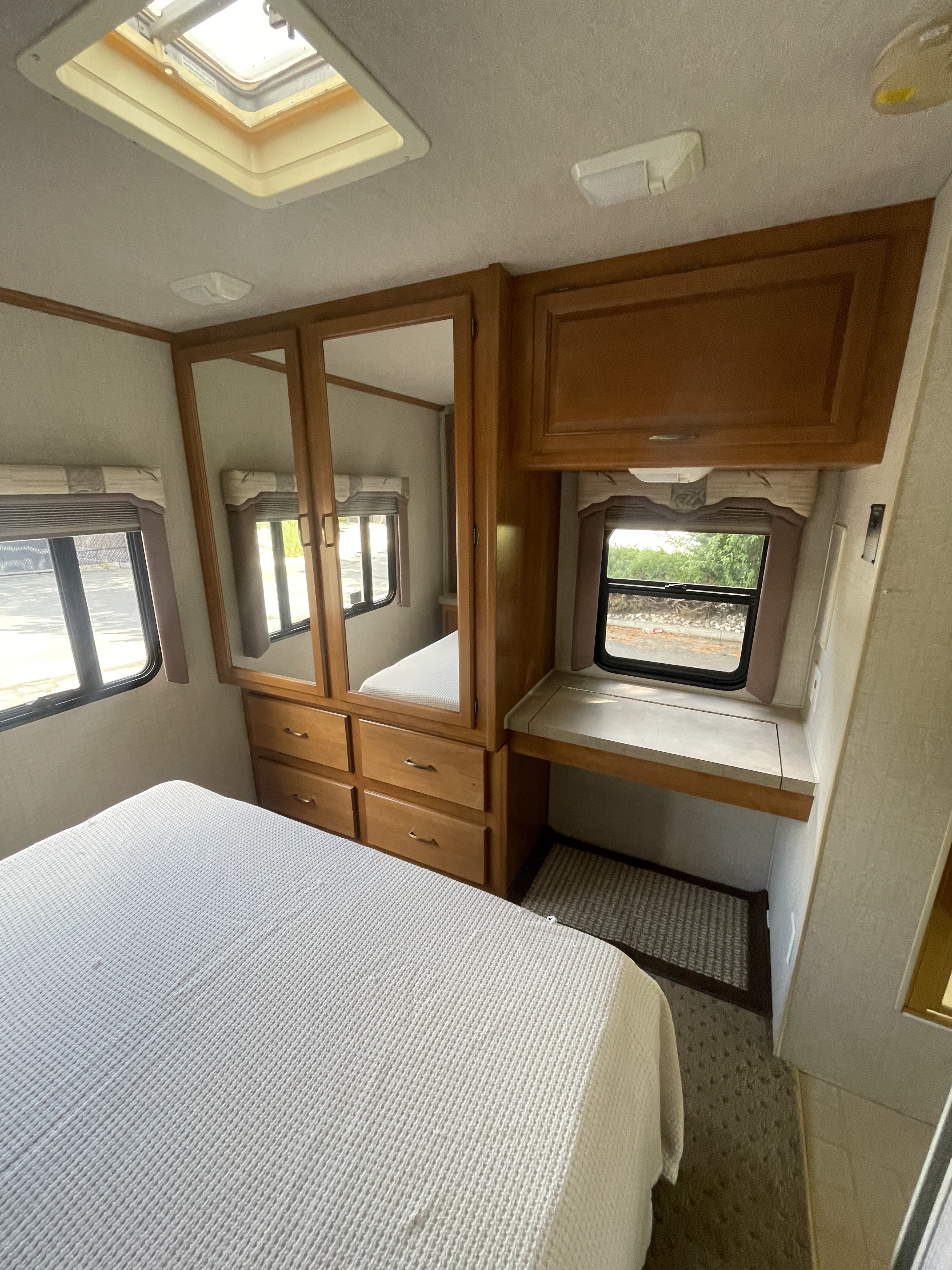 RV rental bedroom interior, featuring a bed, mirrored wardrobe, and a built-in desk with window.. Fleetwood Tioga Sl 2004