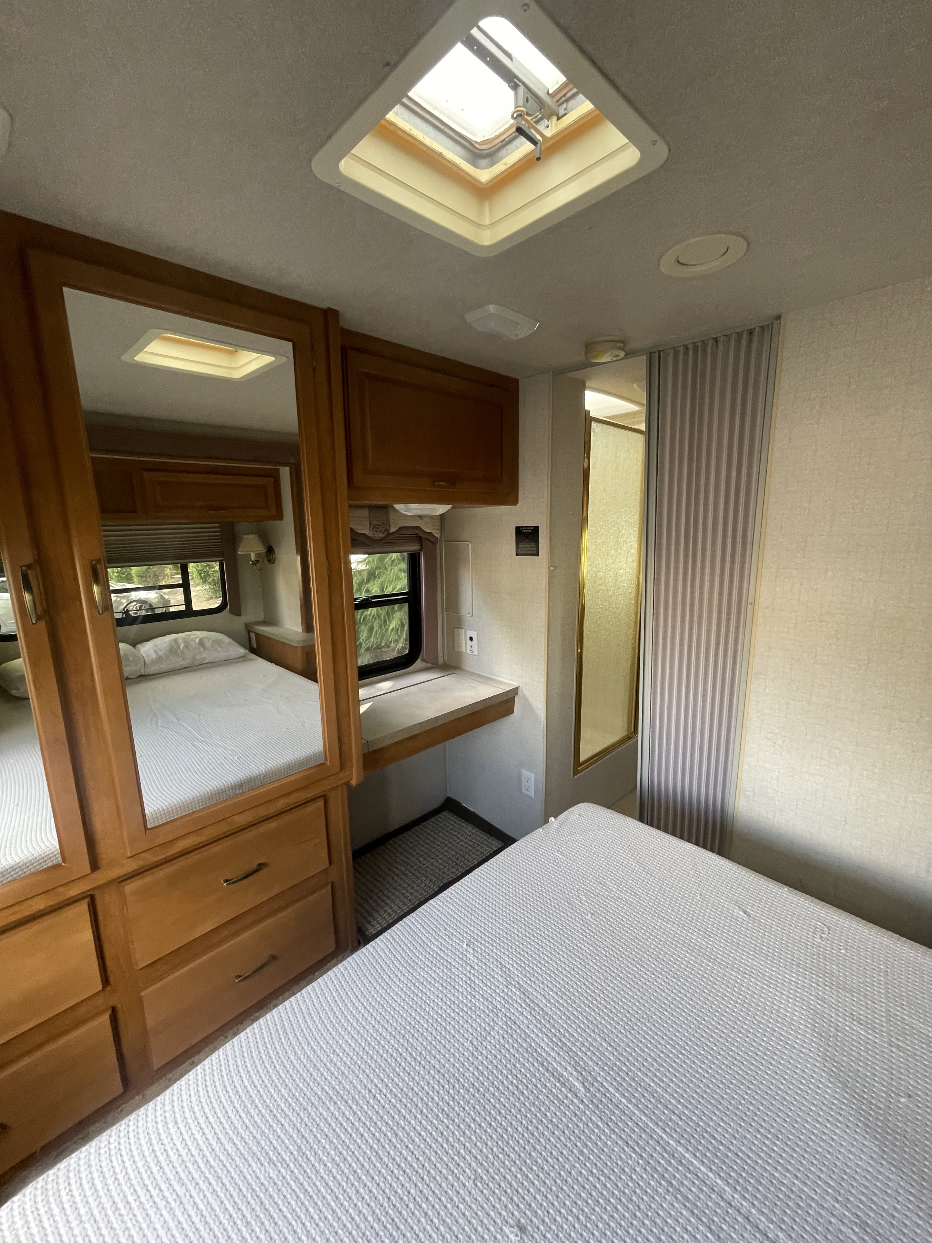 RV rental interior: view of a neat bedroom with white bed, wooden dresser/mirror, skylight, and adjacent shower.. Fleetwood Tioga Sl 2004