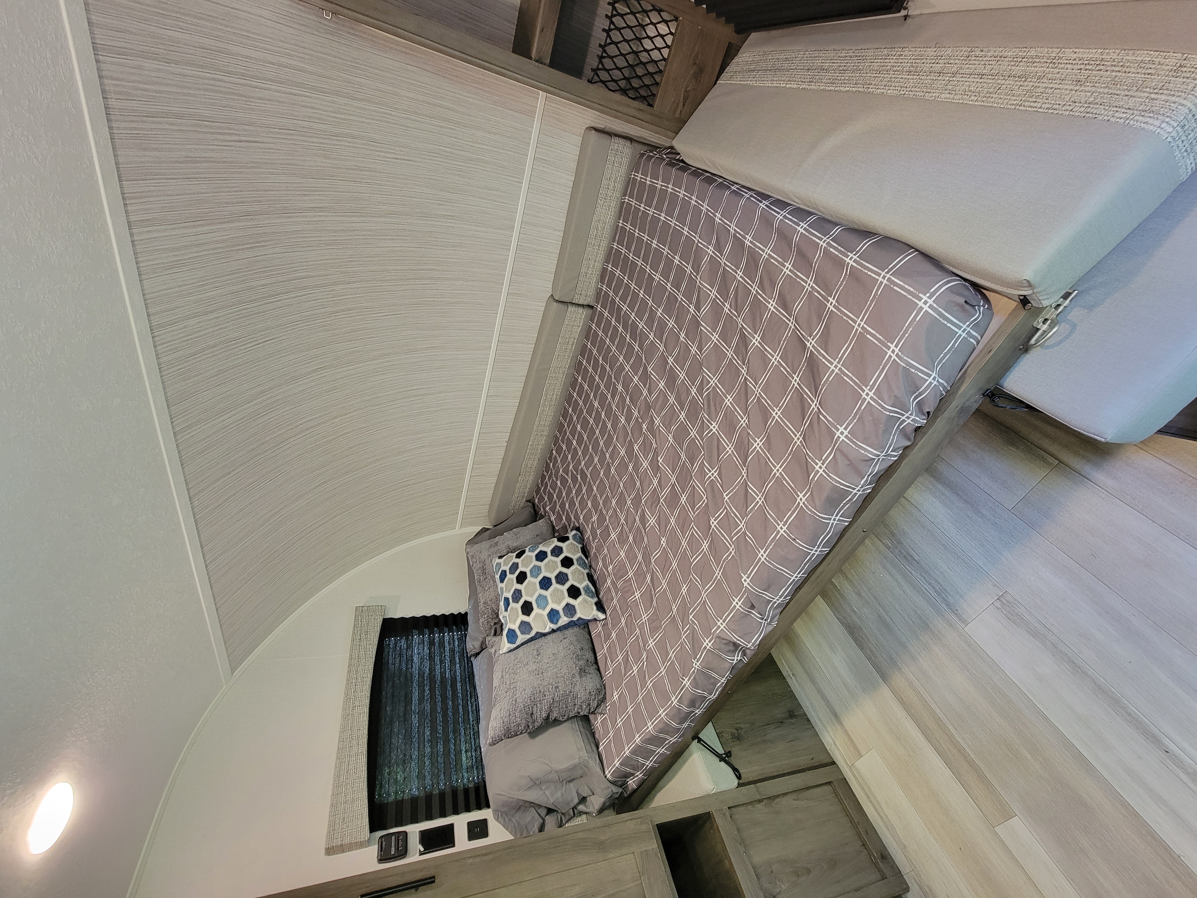 Modern RV rental sleeping area featuring checkered bedding, patterned pillows, and light wood flooring.. Clipper Ultra Lite 2022