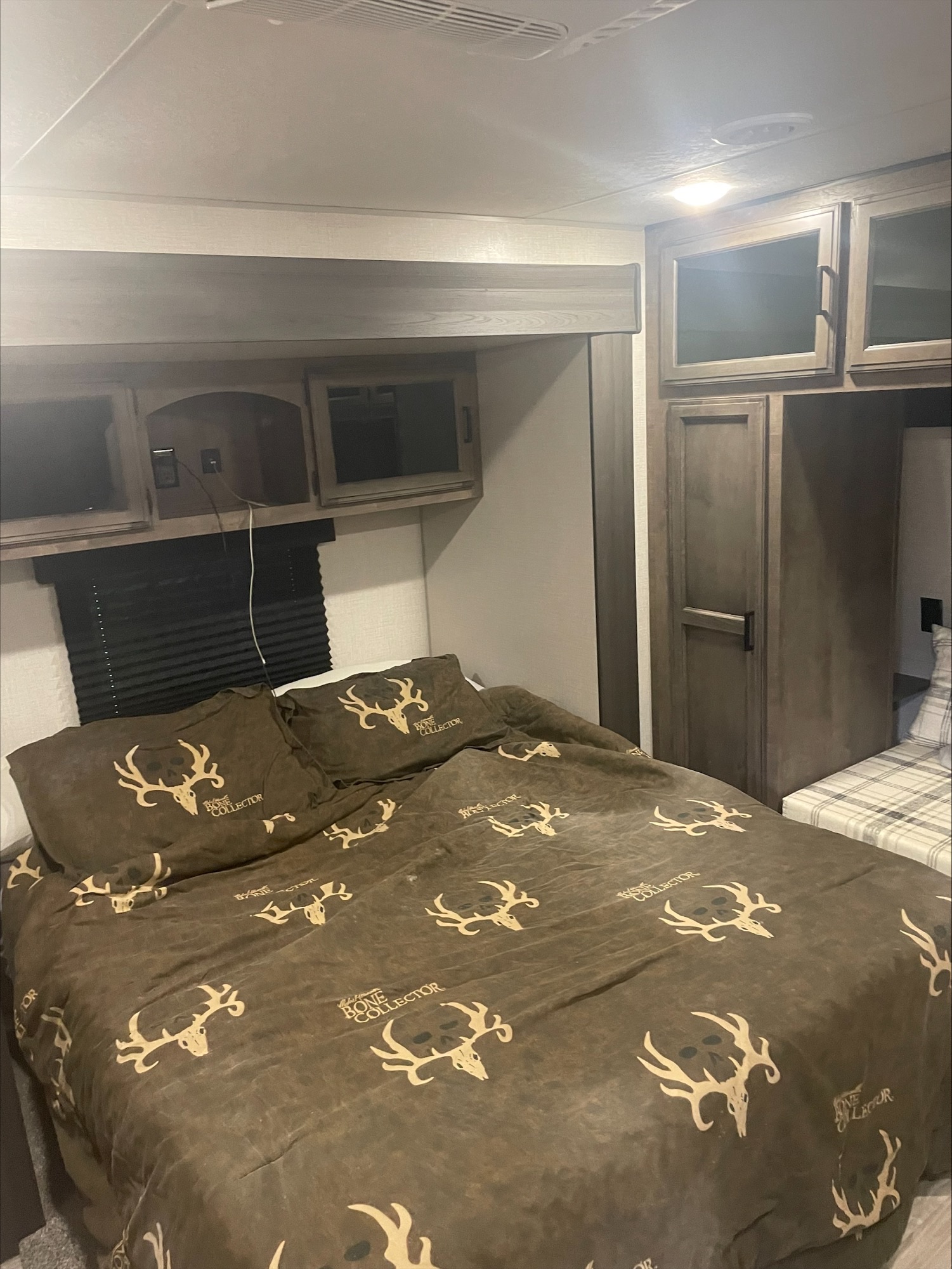 RV rental bedroom with unique 'Bone Collector' deer skull bedding, overhead cabinets, and compact storage for a travel-ready interior.. Sport Trek Sport Trek Trailer 2022
