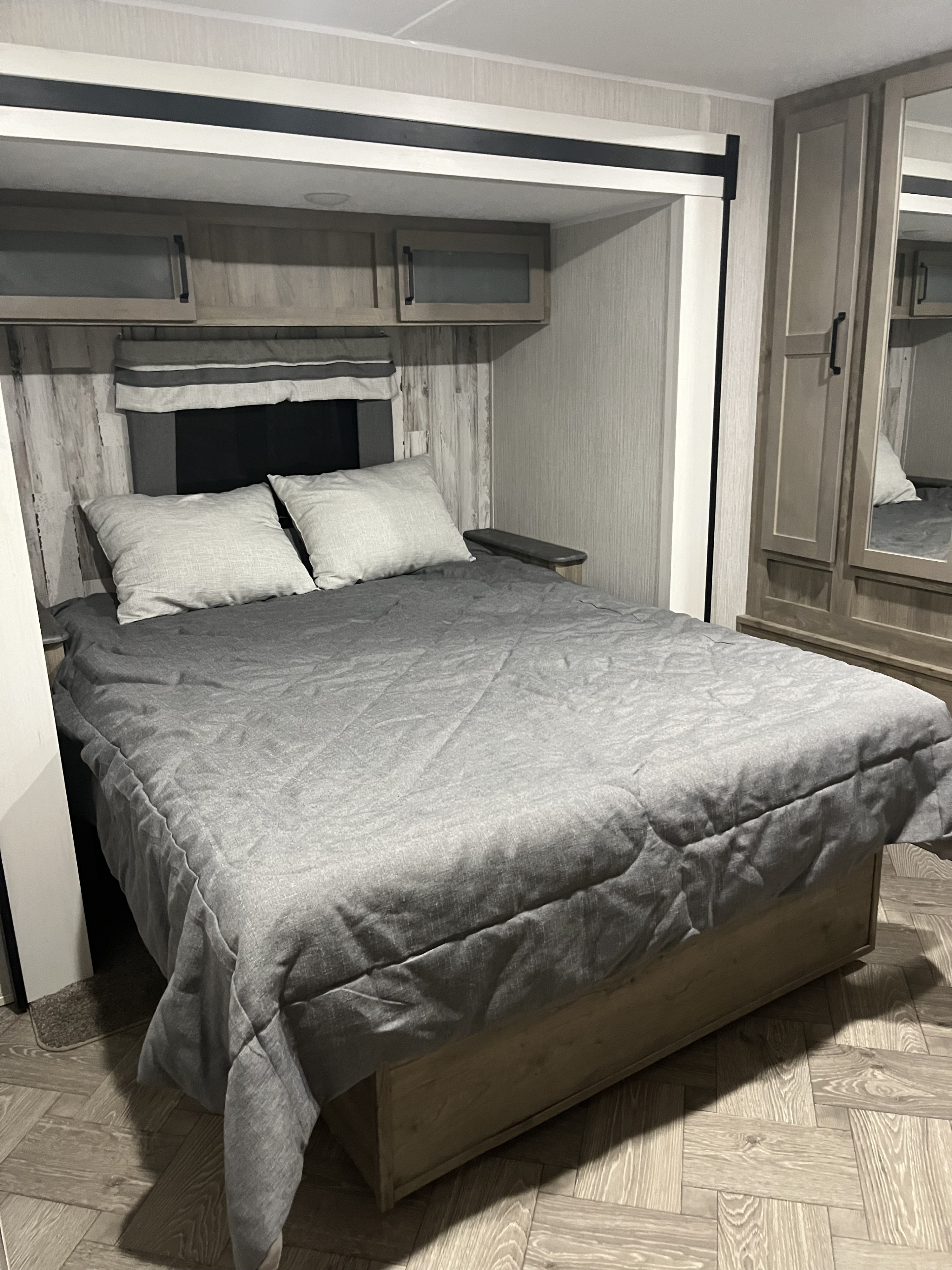 This RV rental bedroom features a comfy bed with gray bedding, overhead cabinets, and mirrored wardrobe.. Forest River Palomino Puma 2021