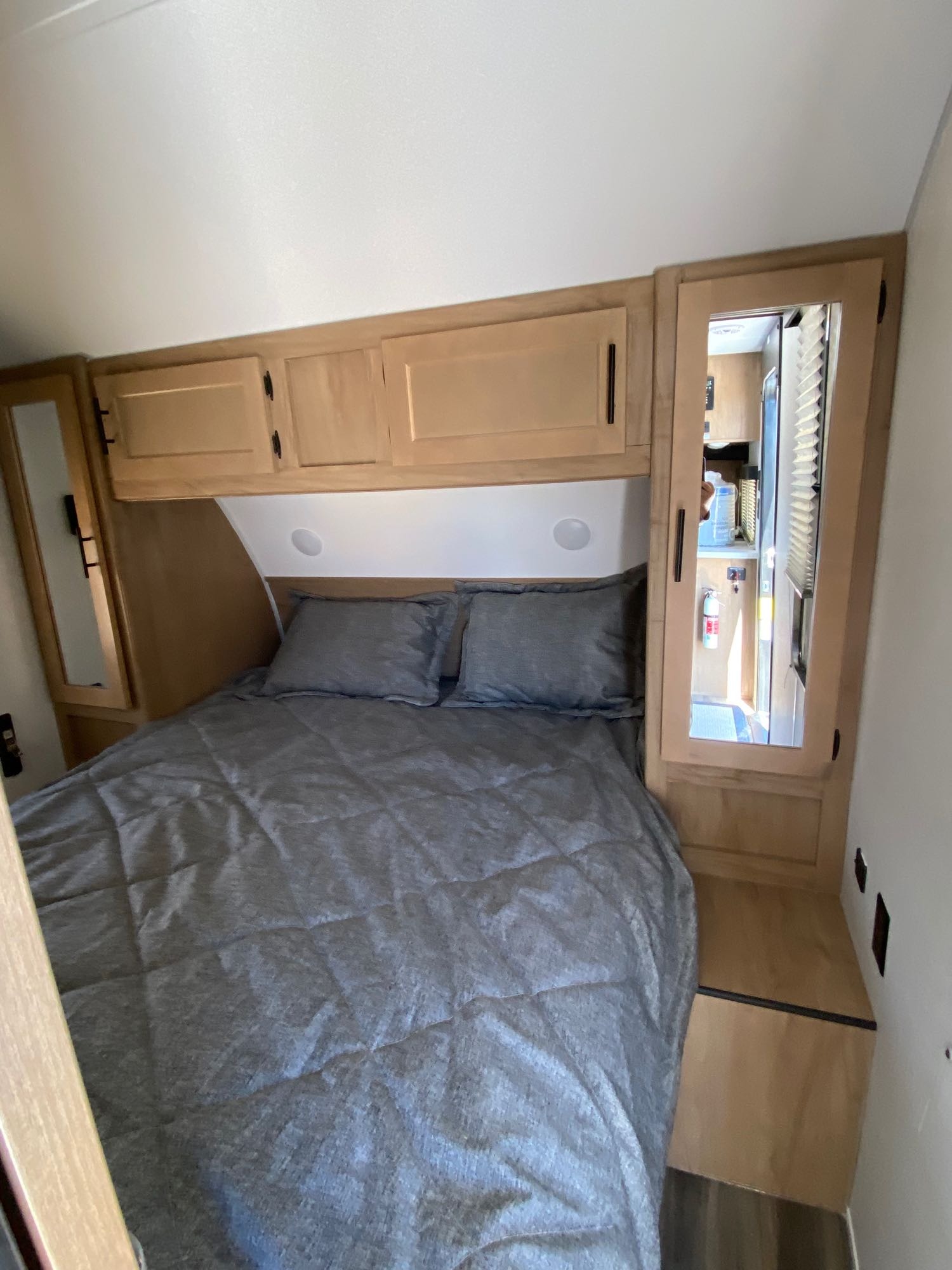 Cozy RV rental bedroom with gray bedding, overhead cabinets, and a mirrored closet reflecting the compact interior.. Forest River 23DBH 2023