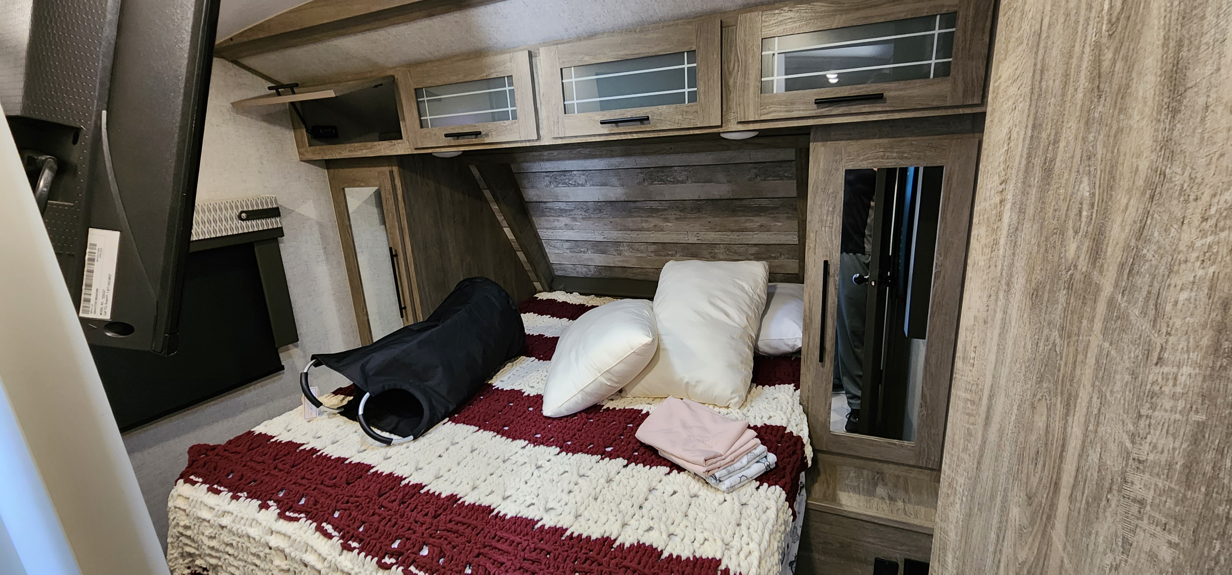 RV rental bedroom showcasing a cozy bed with striped blanket, overhead storage, mirrored closet, and wall-mounted TV.. Forest River Wildwood Heritage Glen 2020