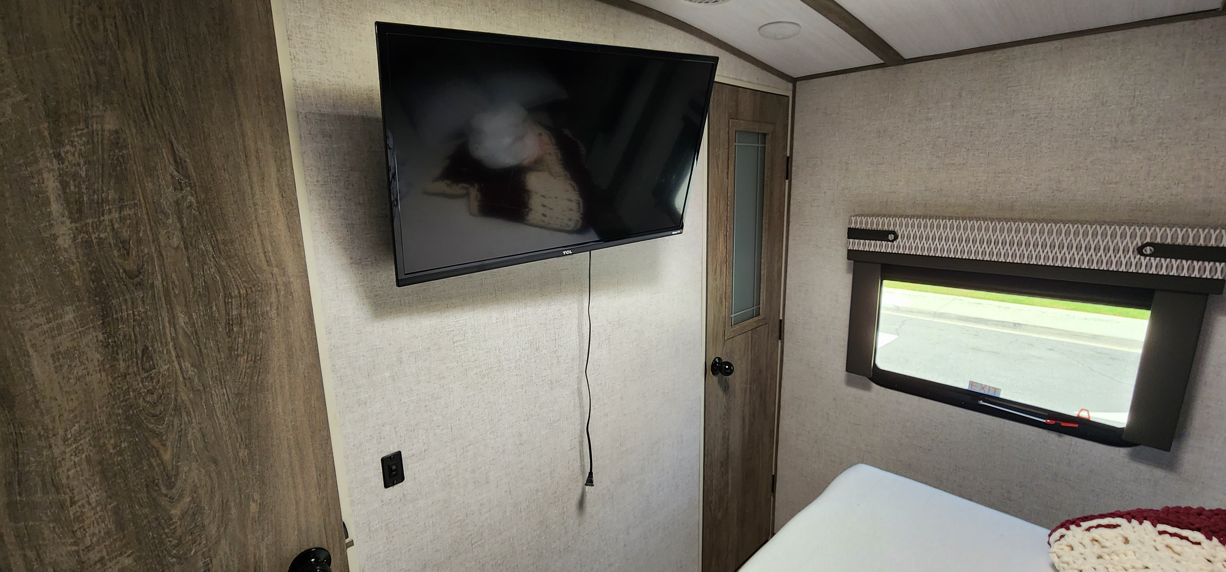 Cozy RV rental bedroom interior, with a wall-mounted TV, window showing an outdoor view, and a wooden door.. Forest River Wildwood Heritage Glen 2020